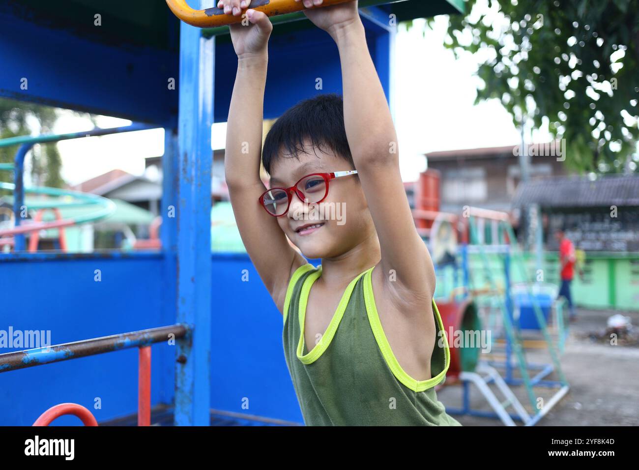 Un enfant joyeux pend de l'équipement de terrain de jeu, profitant du jeu en plein air. Cette scène vibrante capture l'essence de l'enfance, de l'exercice et du bonheur. Banque D'Images