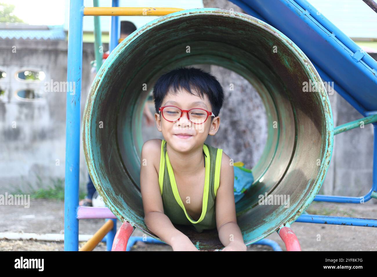Un enfant joyeux est vu souriant tout en jouant à l'intérieur d'un tube coloré de terrain de jeu, incarnant le bonheur et le plaisir de plein air insouciant dans un cadre vibrant. Banque D'Images