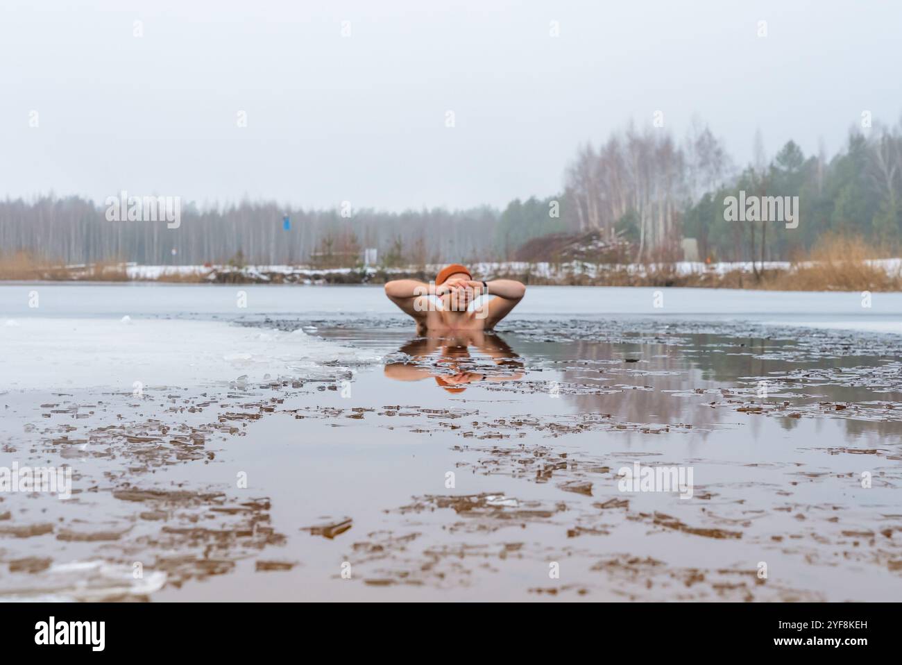 Un homme prend un plongeon dans un lac gelé, entouré par la nature enneigée, pour une expérience rajeunissante de la natation hivernale Banque D'Images