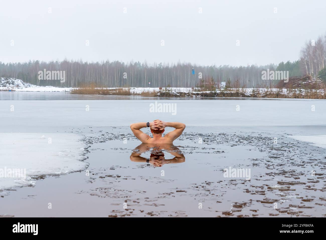 Un homme prend le bain de glace dans le lac gelé, l'eau glacée offrant une expérience rafraîchissante et revigorante pendant la baignade hivernale Banque D'Images