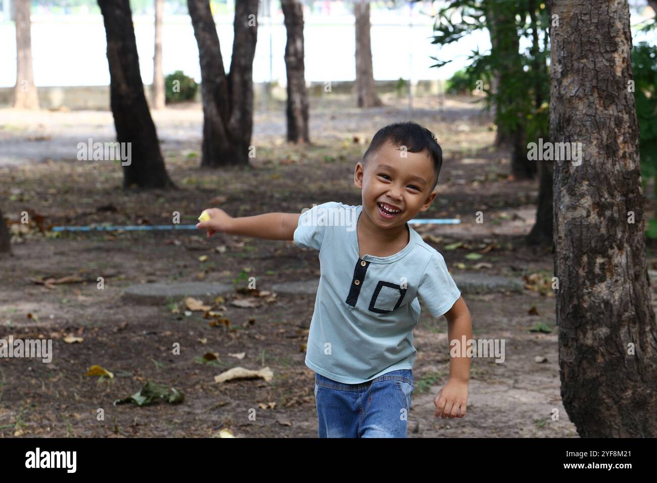 Un enfant joyeux court à travers un parc ensoleillé, mettant en valeur le bonheur pur et l'énergie. Le cadre naturel renforce l'esprit insouciant du jeu d'enfance. Banque D'Images