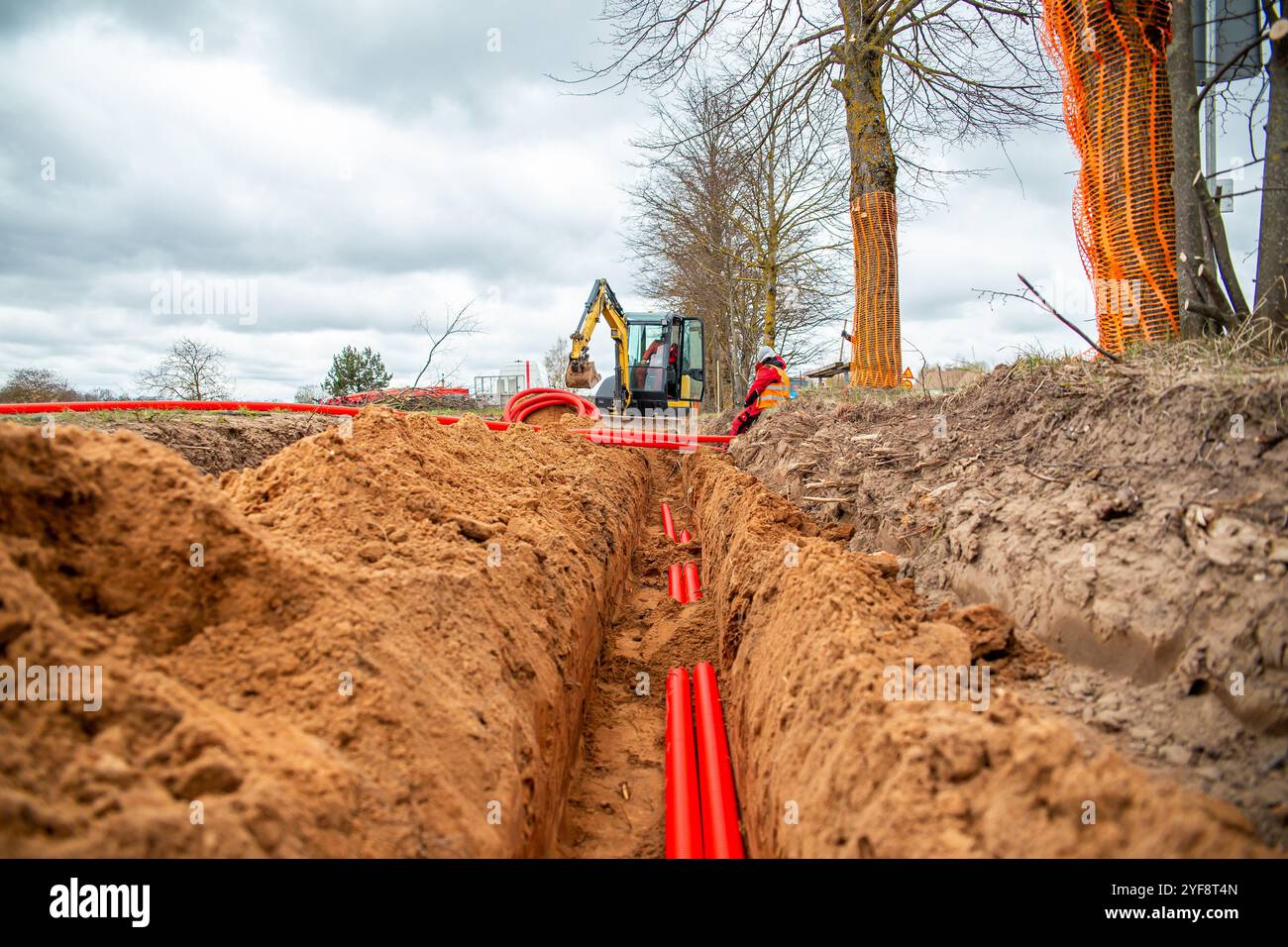Les câbles de réseau dans le tuyau ondulé rouge sont enterrés sous terre dans la rue. installation d'infrastructure de câbles électriques souterrains. Banque D'Images