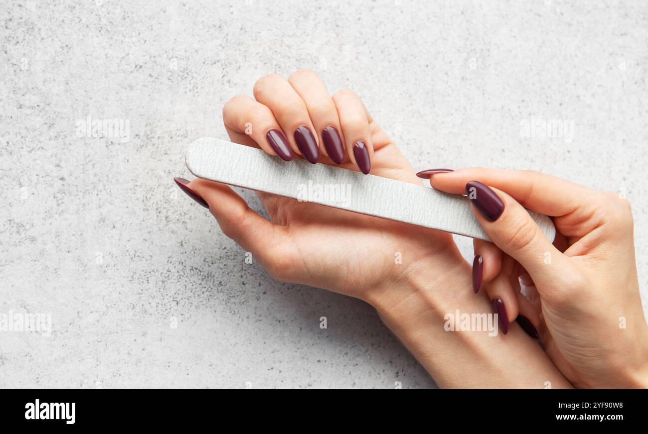 Une personne remplit soigneusement ses ongles à la maison, en utilisant une lime à ongles pour façonner et lisser les bords, créant un look élégant pour une manucure. Banque D'Images