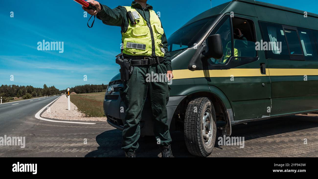 Officier de la circulation en gilet haute visibilité tenant une matraque pour le contrôle de la route près d'un véhicule de patrouille, avec équipement de sécurité Banque D'Images