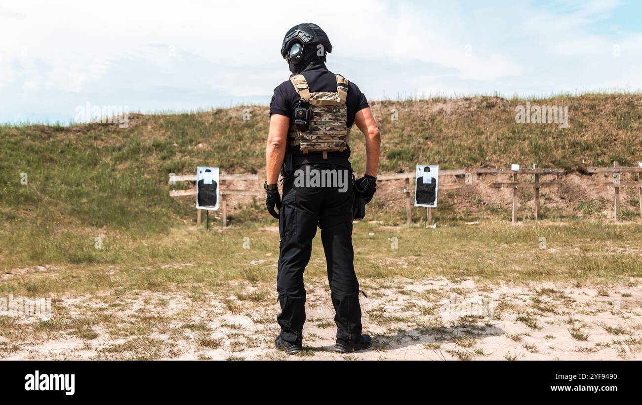 Agents des forces spéciales en équipement tactique pratiquant l'entraînement aux armes à feu dans un champ de tir extérieur sous un ciel nuageux Banque D'Images