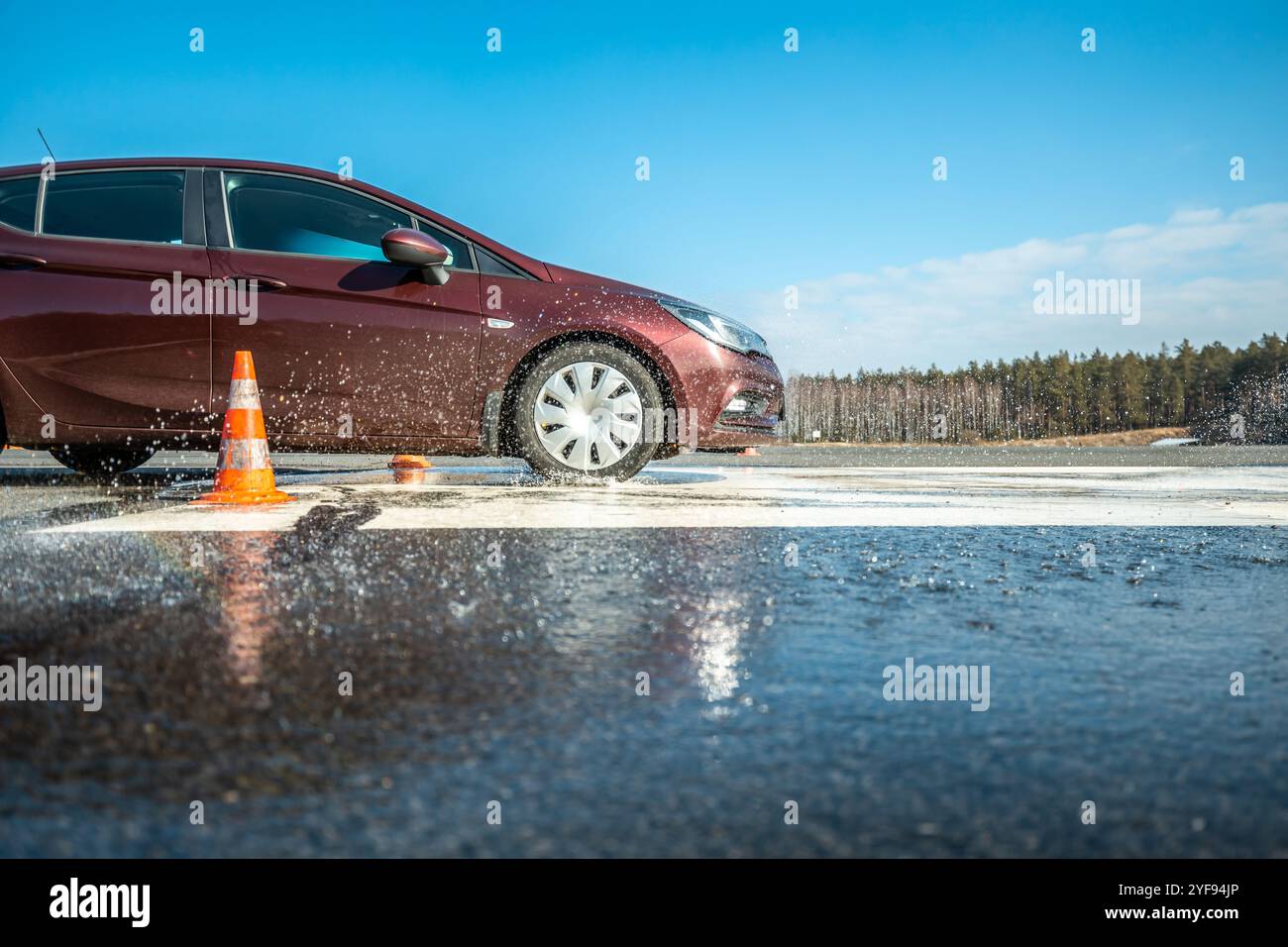 essai de freinage dynamique des véhicules sur chaussée mouillée avec éclaboussures d'eau et cônes orange, évaluation de la sécurité des véhicules dans un environnement contrôlé Banque D'Images