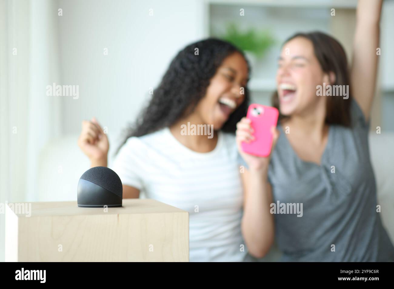 Amis interraciaux heureux chantant à la maison avec un haut-parleur intelligent jouant de la musique Banque D'Images