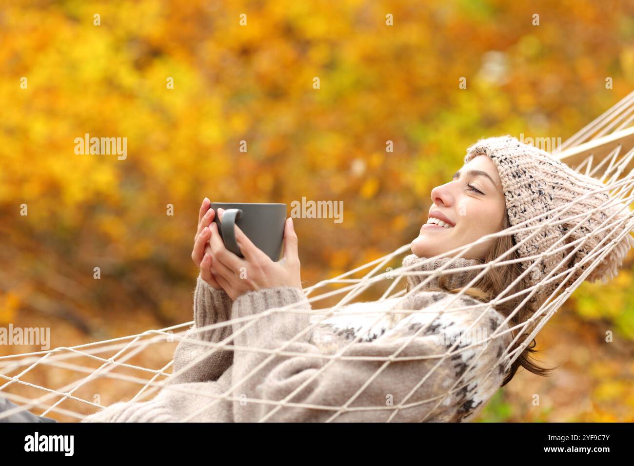 Profil d'une femme heureuse reposant sur un hamac buvant du thé en automne Banque D'Images