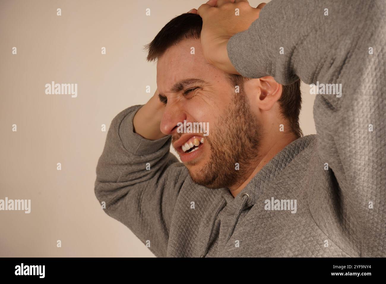 L'homme en dépression. Portrait d'un jeune homme fermant les oreilles par les mains et gardant les yeux fermés tout en étant isolé sur gris. Photo de désespéré agacé Banque D'Images