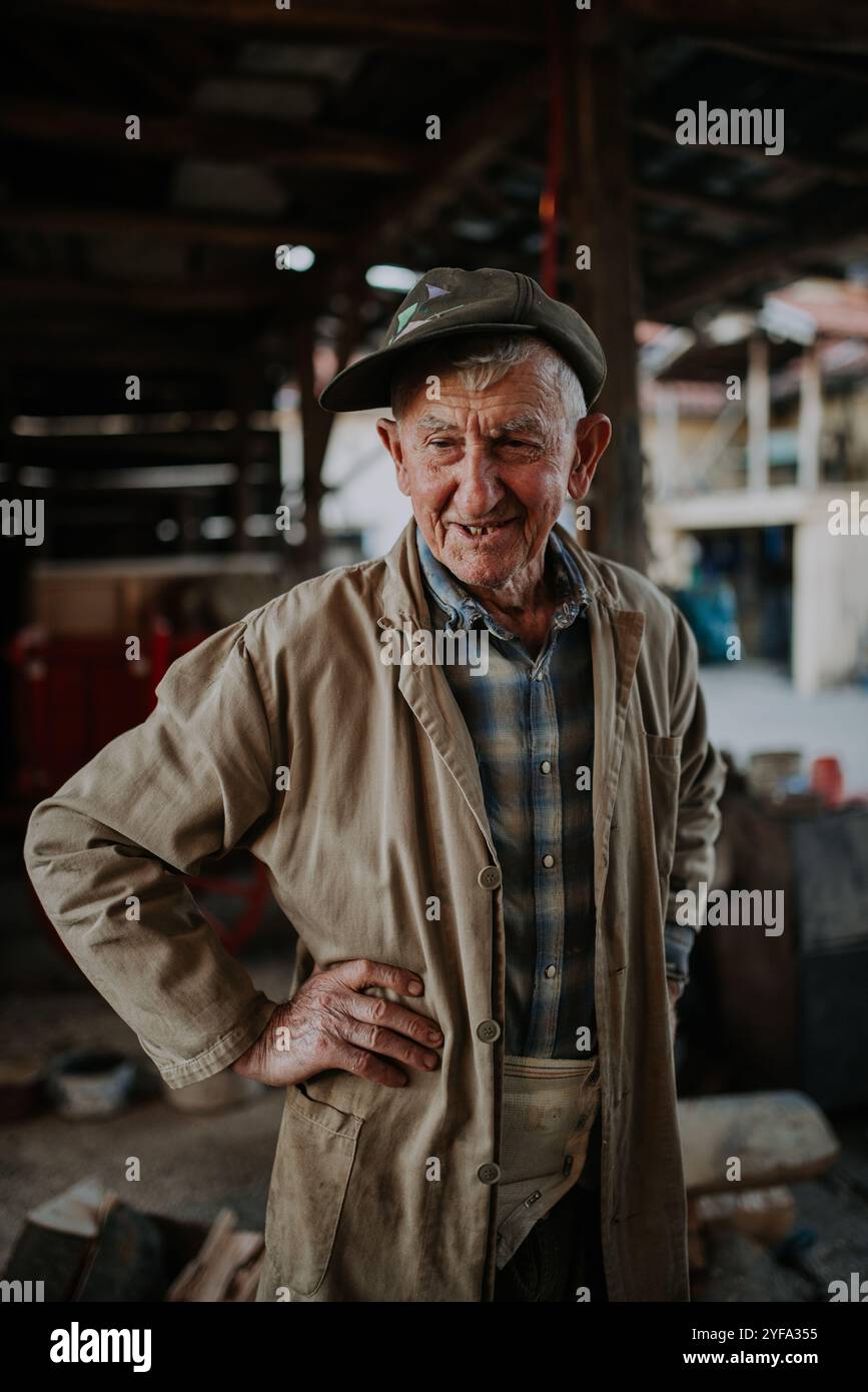 Vieil homme en vêtements de travail debout dans sa grange. Banque D'Images