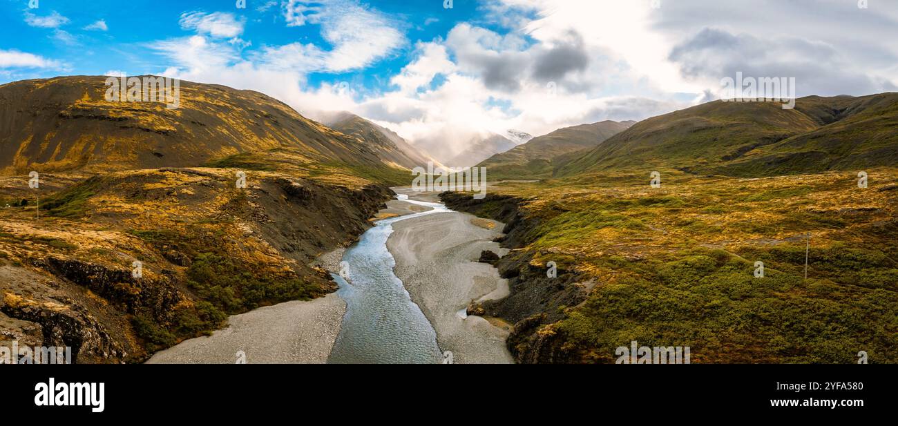 Superbe vue aérienne d'une rivière islandaise serpentant à travers une vallée entourée de collines escarpées et de montagnes brumeuses, capturant la beauté brute et sereine Banque D'Images