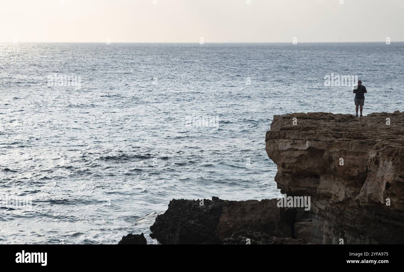 Silhouette d'une personne au bord d'une falaise rocheuse au coucher du soleil dans l'océan Banque D'Images