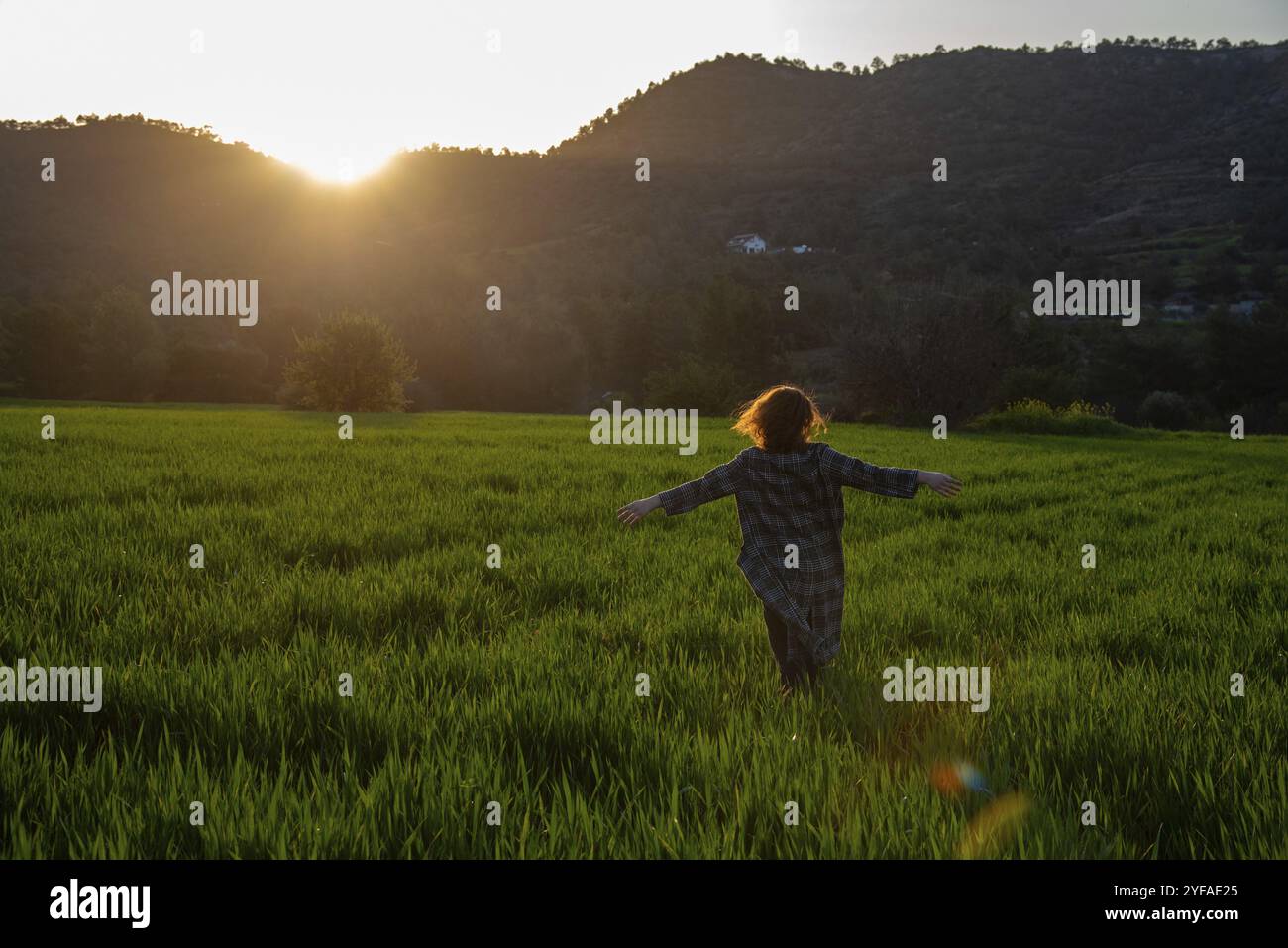 Femme avec un long manteau et les bras tendus profitant du coucher du soleil sur la prairie verte. Les gens actifs en plein air au coucher du soleil Banque D'Images