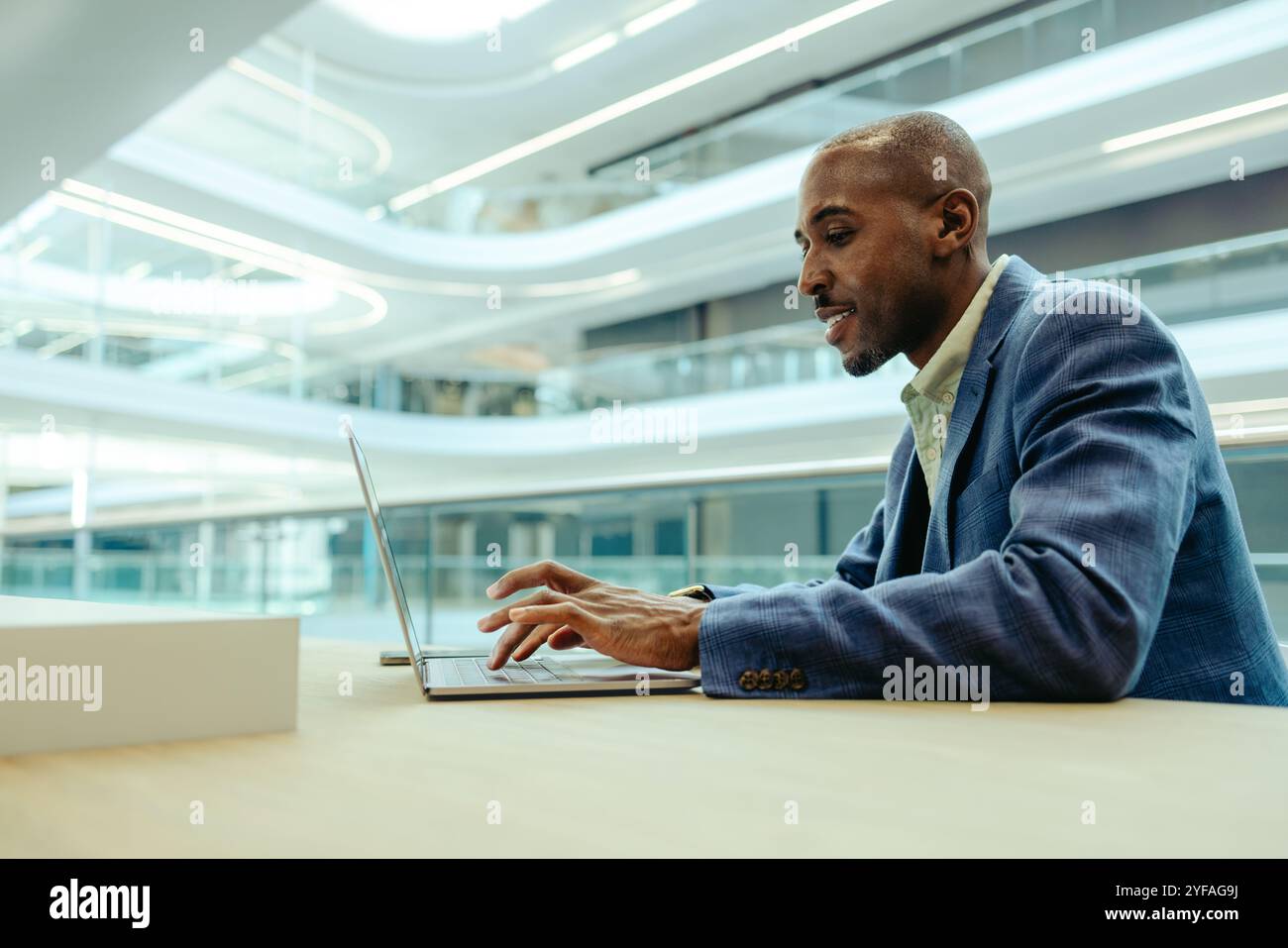 Homme d'affaires professionnel travaillant sur un ordinateur portable dans un bureau moderne et lumineux. Le cadre est corporatif, avec une architecture élégante et un éclairage naturel. HE ap Banque D'Images
