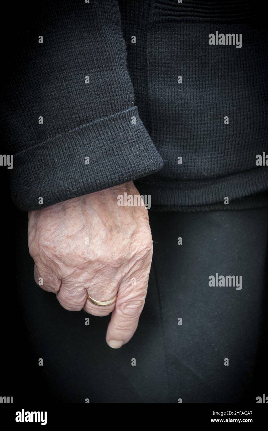 Main d'une femme aînée avec des vêtements noirs, portant une bague de mariage sur un de ses doigts Banque D'Images