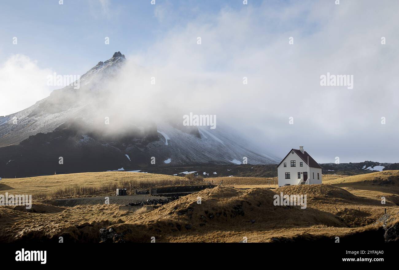 Belle maison solitaire dans le petit village de pêcheurs d'Arnarstapi et falaise de montagne couverte de neige à Snaefellsnes péninsule en Islande Banque D'Images