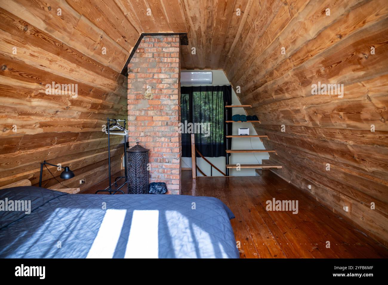 Chambre rustique en bois avec cheminée en briques apparentes et mobilier en bois minimaliste, éclairée par la lumière du soleil. Banque D'Images