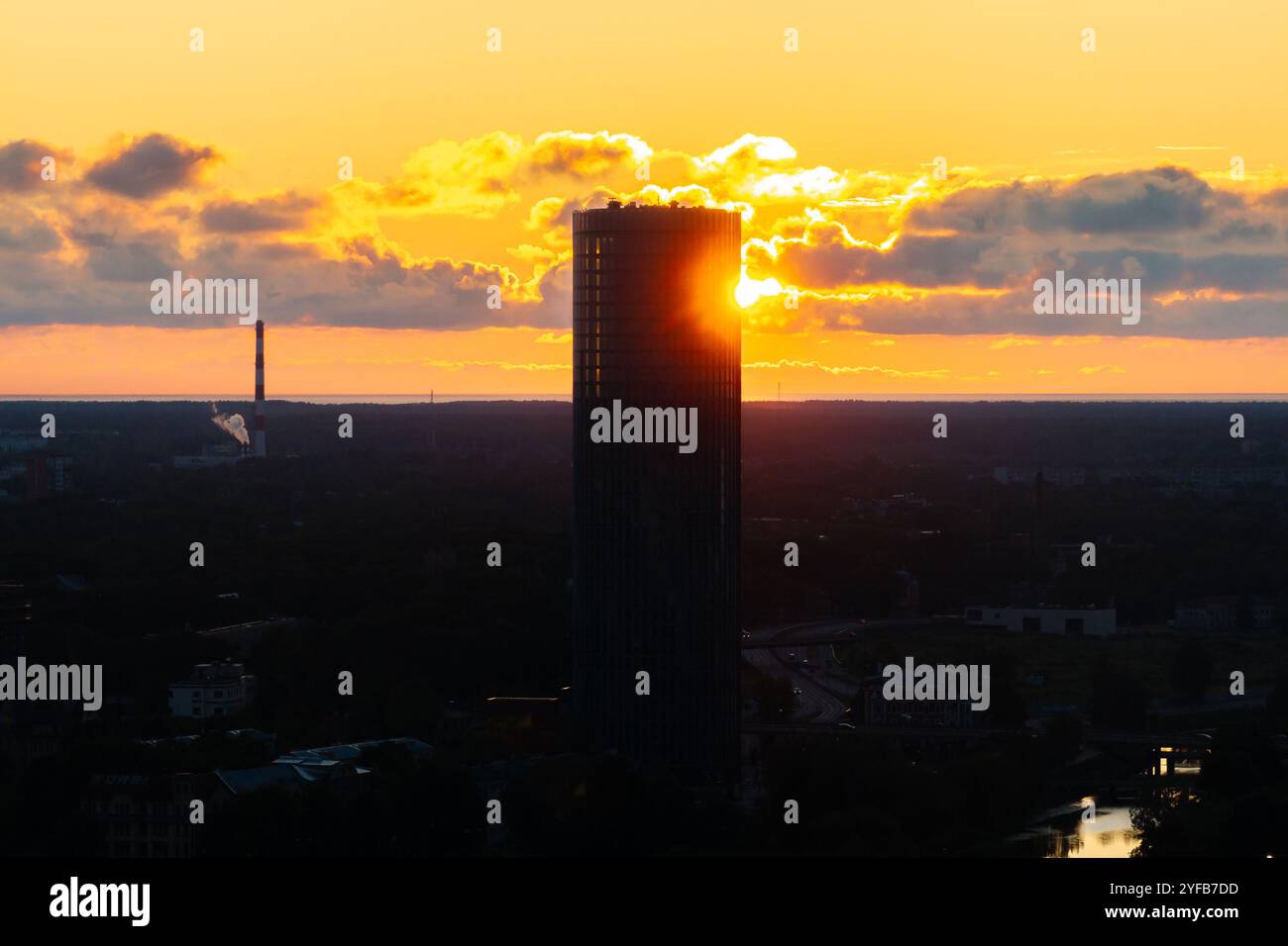 Vue aérienne de Riga au coucher du soleil, avec la rivière Daugava, les ponts et les bâtiments historiques sous un ciel orange chaud. Banque D'Images