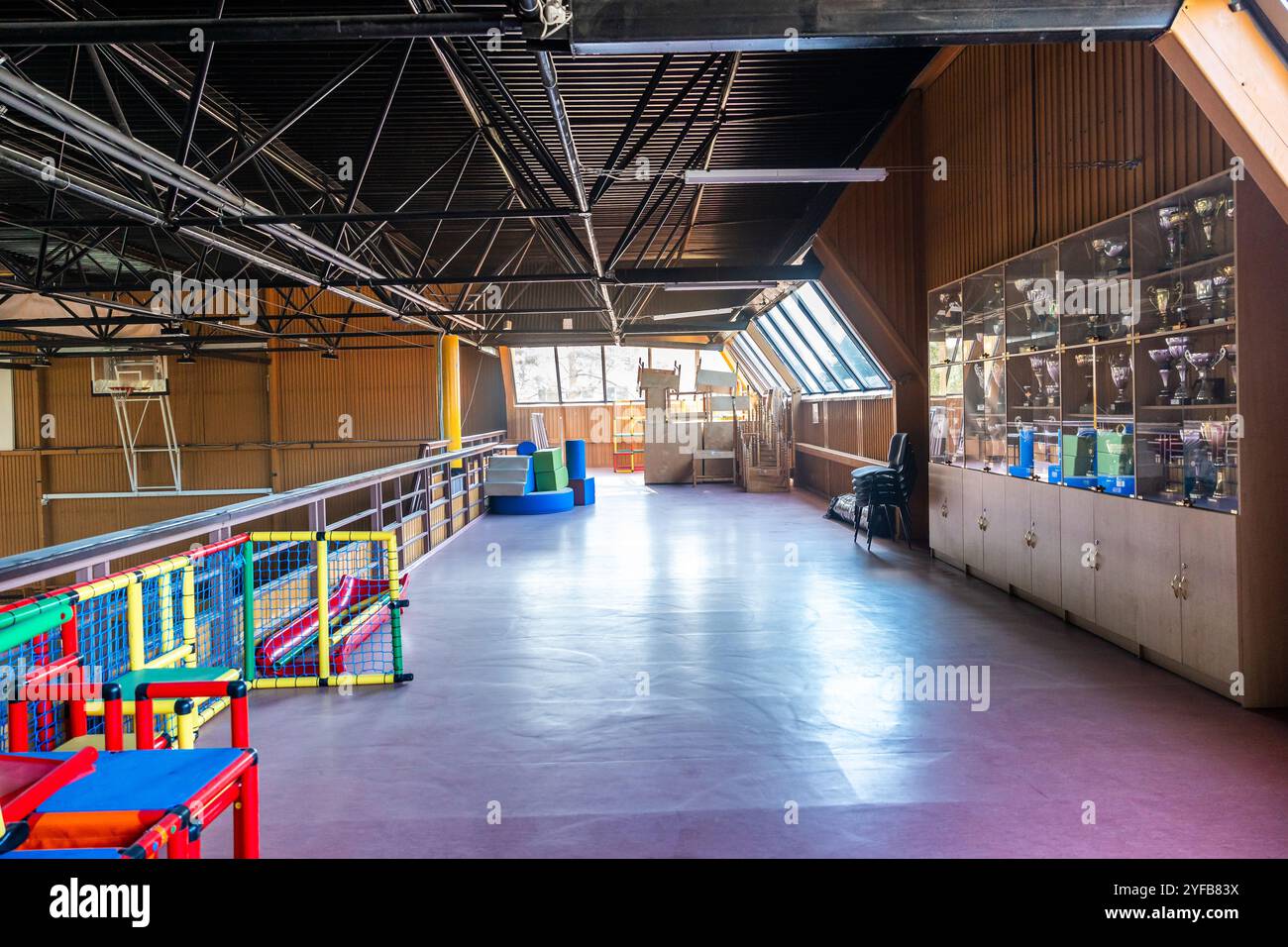 Passerelle surélevée à l’intérieur d’une installation sportive avec armoires à trophées et aire de jeux pour enfants sous un haut plafond. Banque D'Images