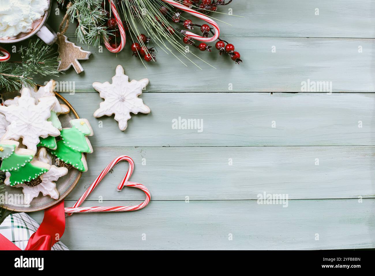 Pose plate de biscuits givrés d'étoile de Noël et de forme d'arbre ou biscuits avec glaçage vert sur une table rustique avec des cannes de bonbon en forme de coeur et guirlande. Banque D'Images