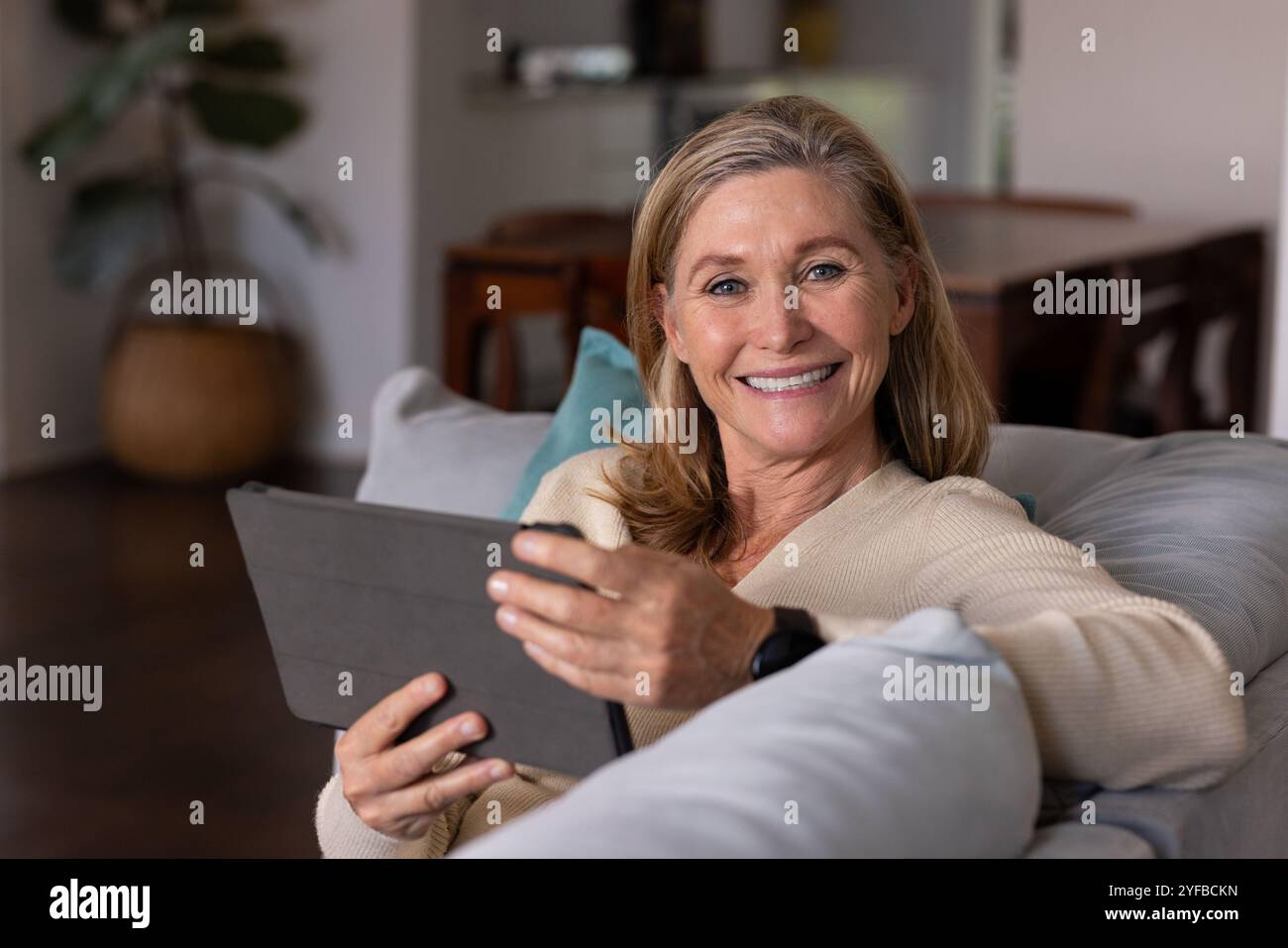 Femme âgée souriante se relaxant à la maison en utilisant une tablette sur un canapé confortable Banque D'Images