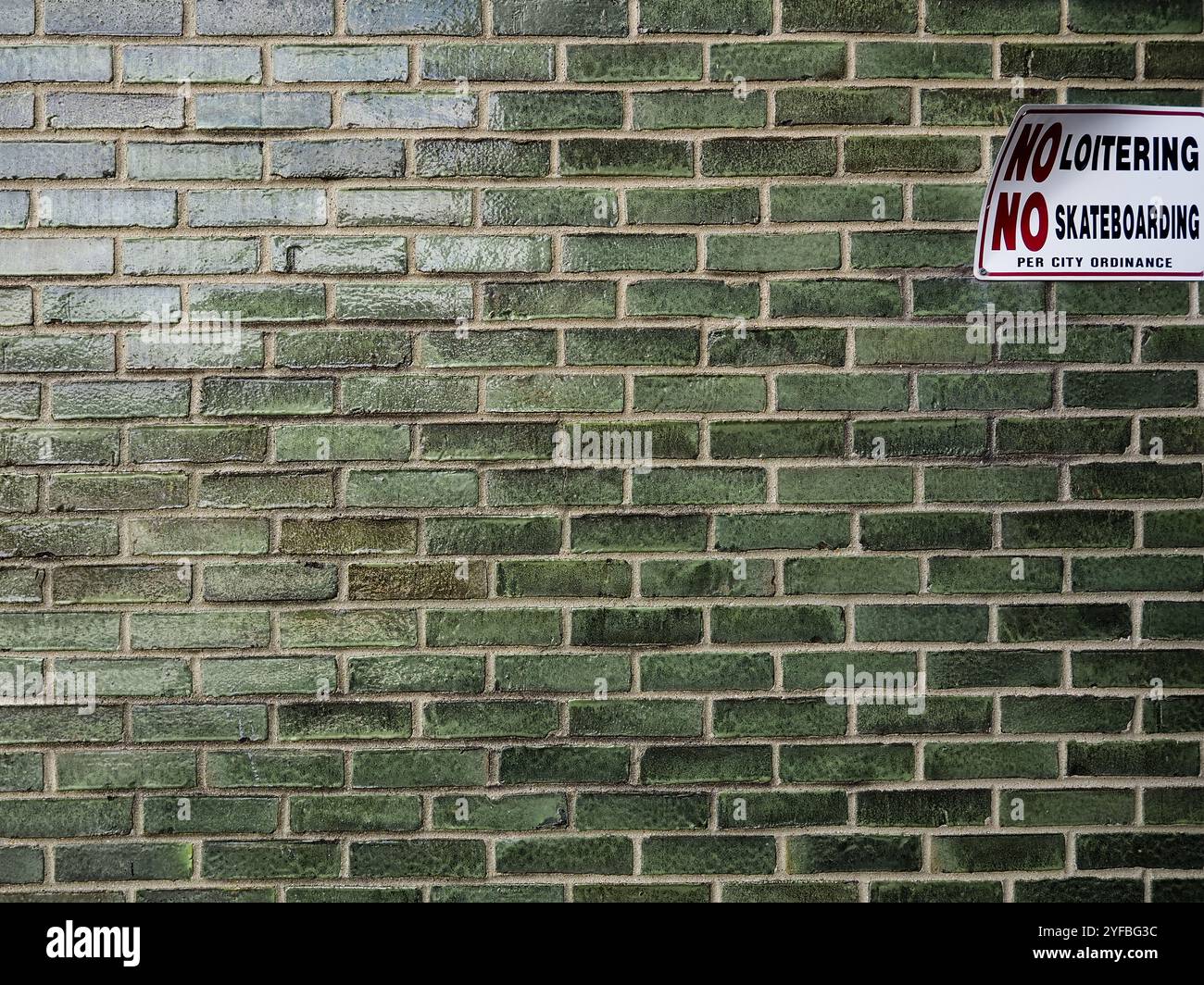 Dans un environnement urbain, un mur de briques vertes se dresse avec un signe clair qui indique pas de flâner et pas de skateboard Banque D'Images