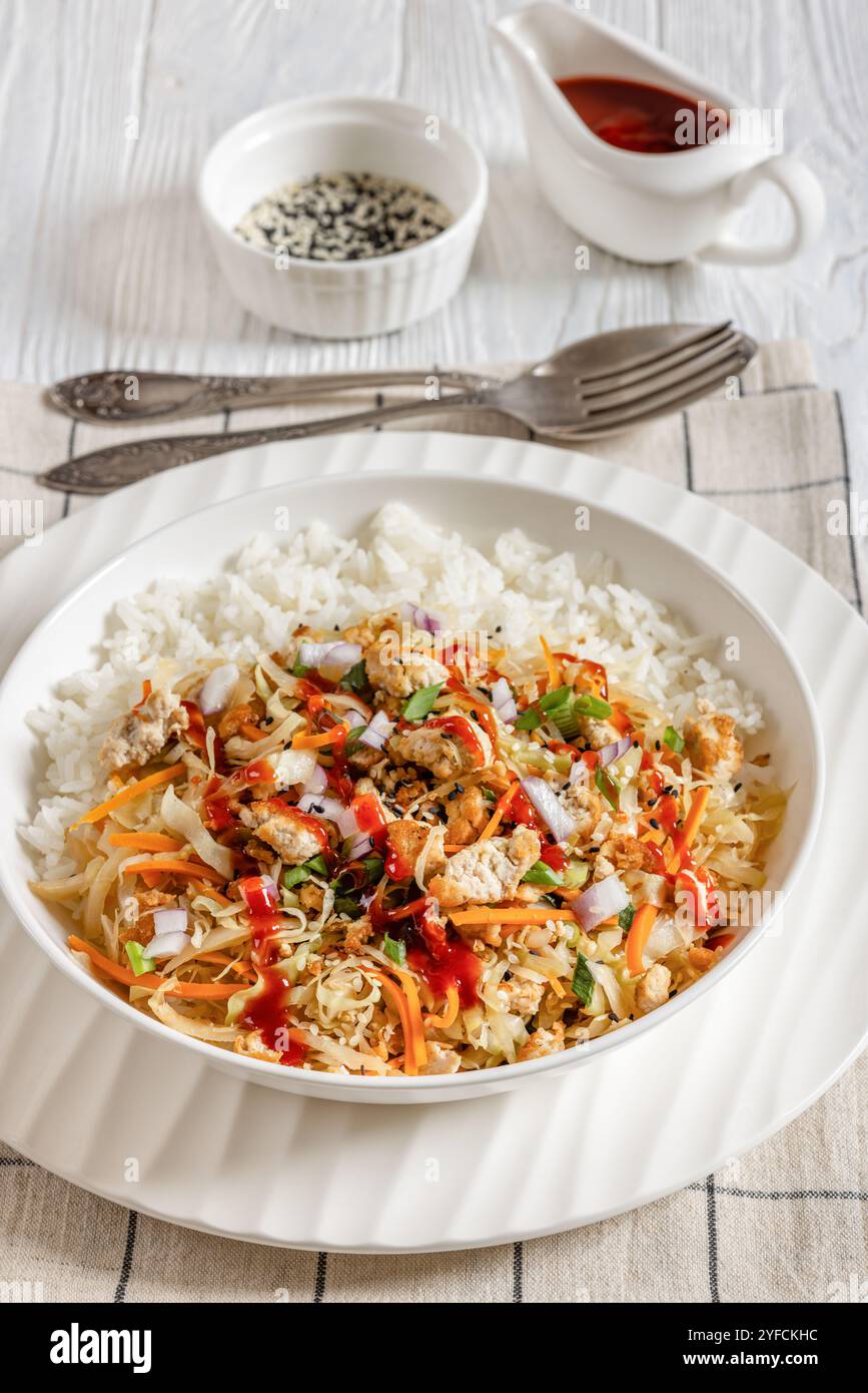 roulé aux œufs de tofu, chou sautés, tofu émietté assaisonné servi dans une sauce sucrée et salée servie sur du riz dans un bol sur une table en bois blanc avec cuillère Banque D'Images