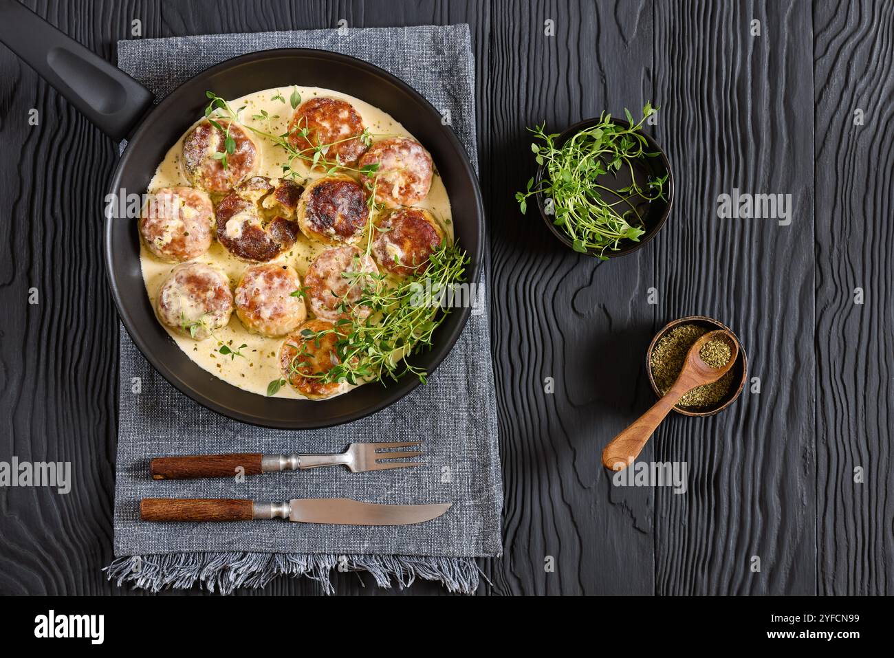 délicieuses rissoles de poulet, galettes dans une riche sauce crème au thym et assaisonnement sur une poêle sur une table en bois noir avec fourchette et couteau, vue horizontale f Banque D'Images