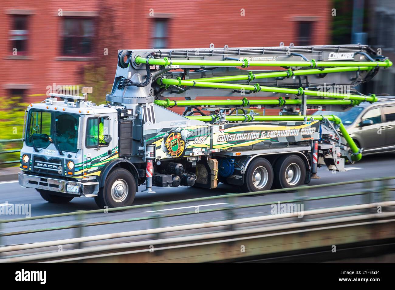 Camion de pompe à béton Mack avec tuyaux verts prolongés conduisant sur une route de ville. Banque D'Images