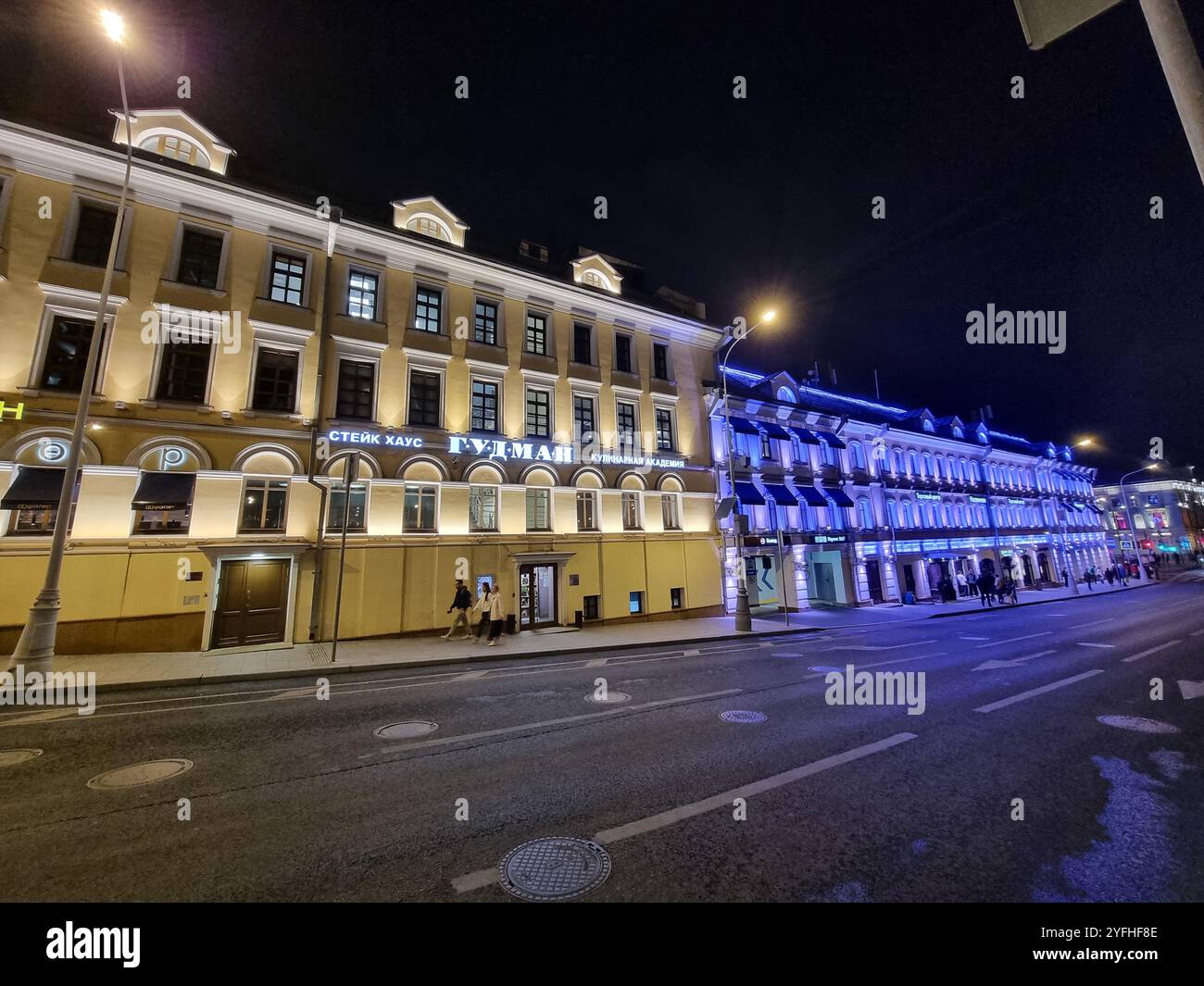 Vue nocturne de bâtiments colorés, jaunes/verts et bleus éclairés le long d'une rue à Moscou, Russie Banque D'Images