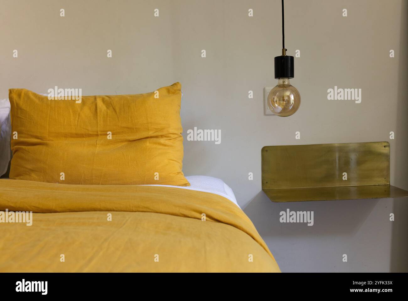 Chambre confortable avec literie moutarde et luminaire suspendu moderne, à la maison Banque D'Images