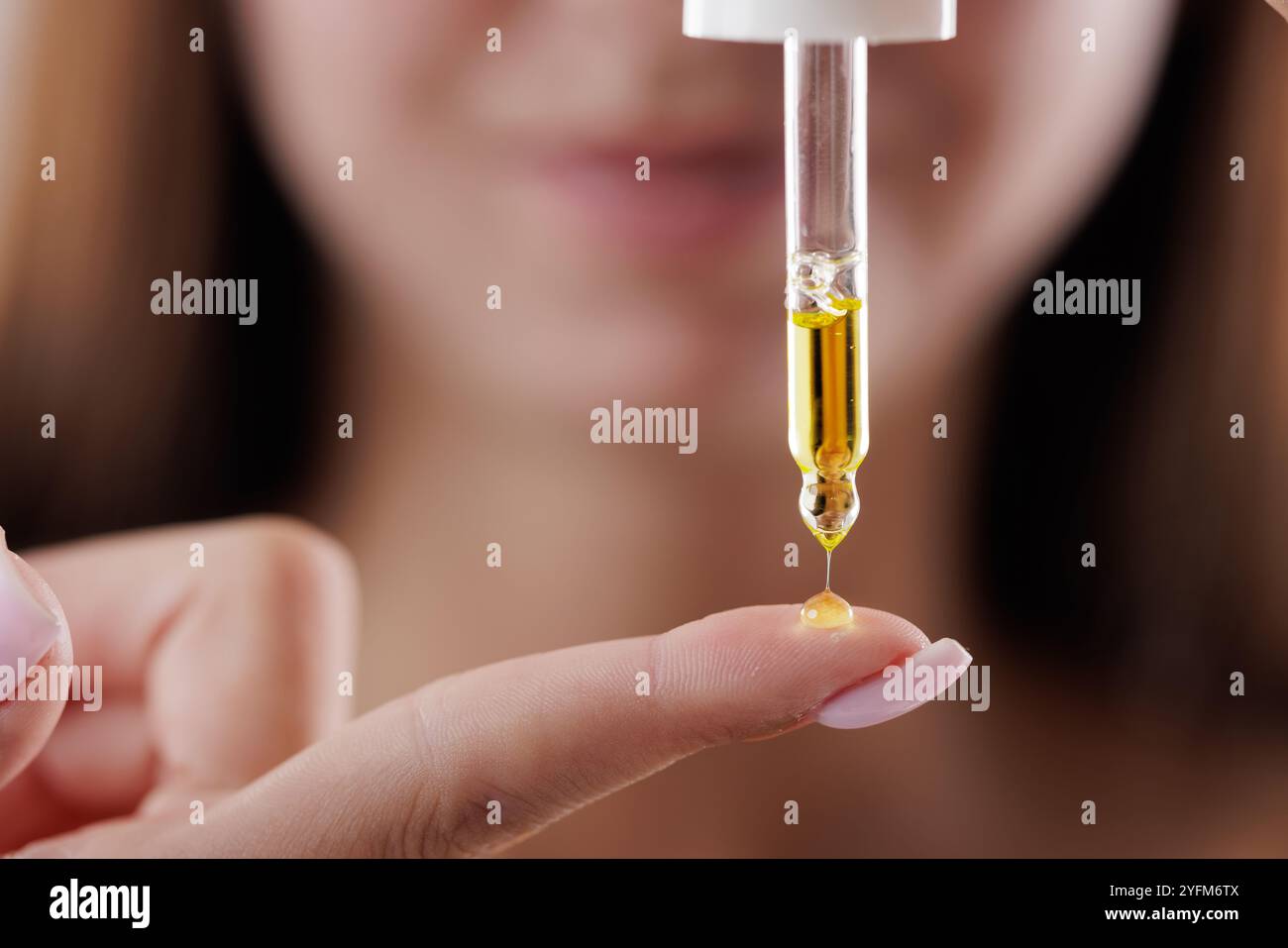 Belle jeune femme appliquant du sérum cosmétique sur son doigt sur fond brun, gros plan Banque D'Images