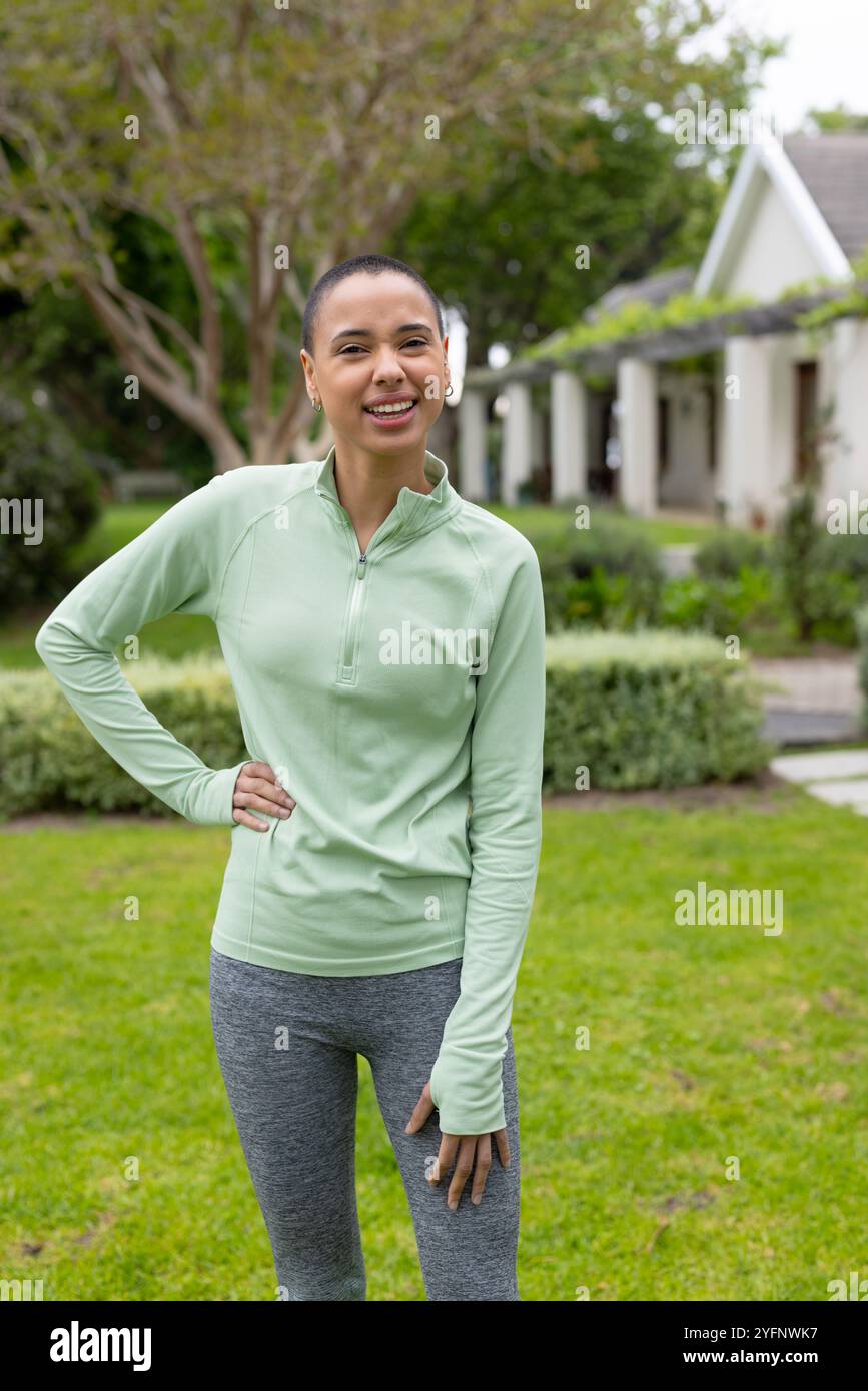 Femme souriante dans les vêtements d'activité profitant de l'exercice en plein air dans le jardin luxuriant Banque D'Images