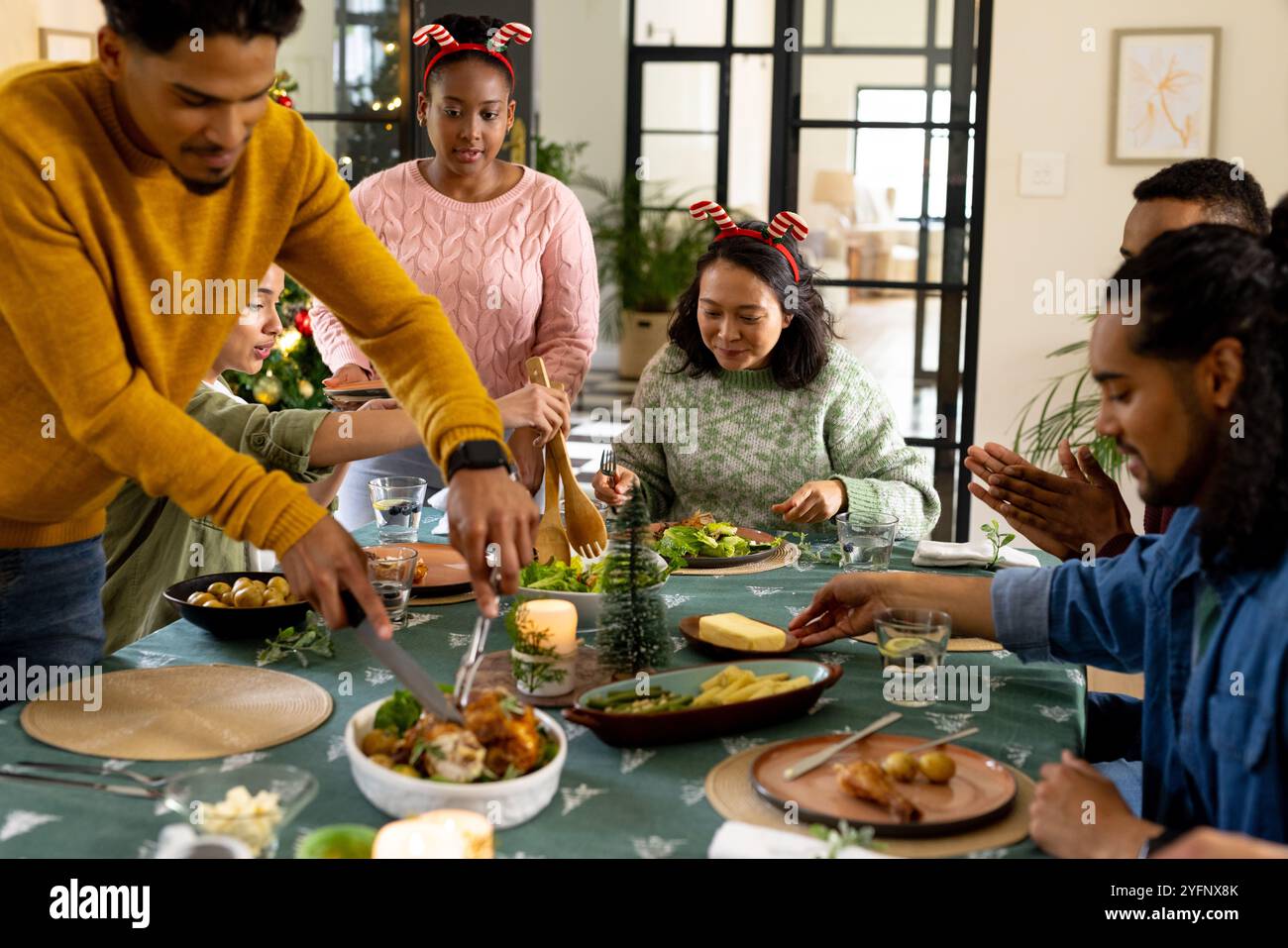 Temps de Noël, jeunes amis multiraciaux profitant d'un repas de fête ensemble, à la maison Banque D'Images