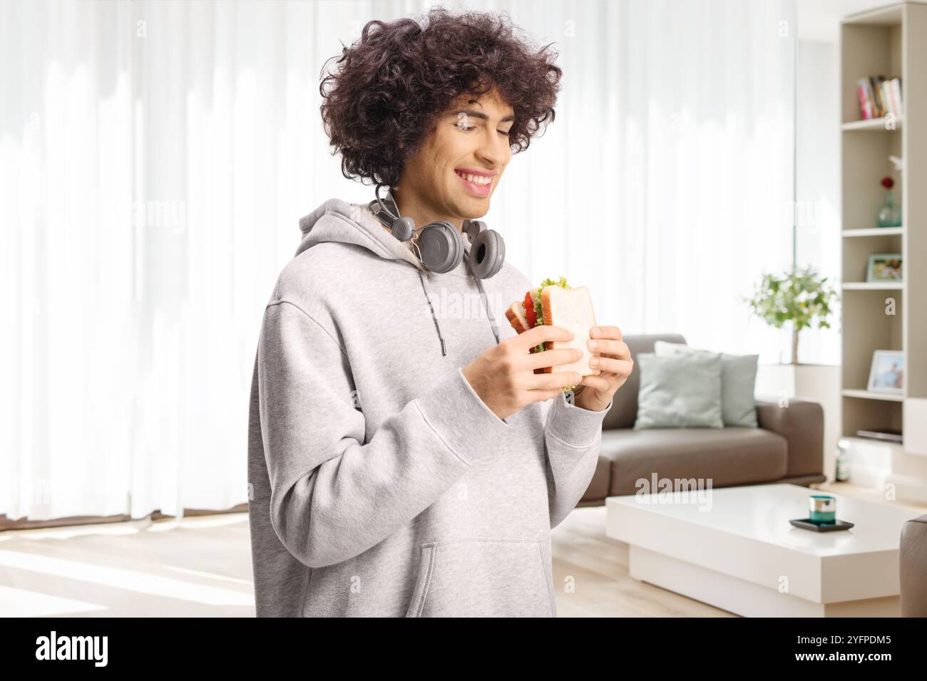 Heureux jeune homme avec des écouteurs tenant un sandwich à la maison dans un salon Banque D'Images