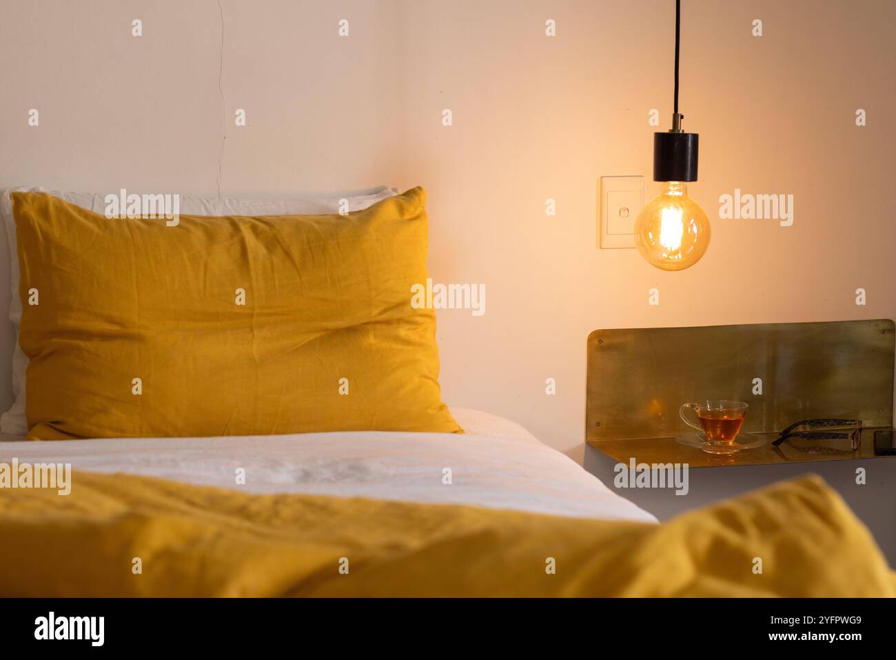 Chambre confortable avec éclairage chaleureux et literie jaune, thé sur table de chevet, à la maison Banque D'Images