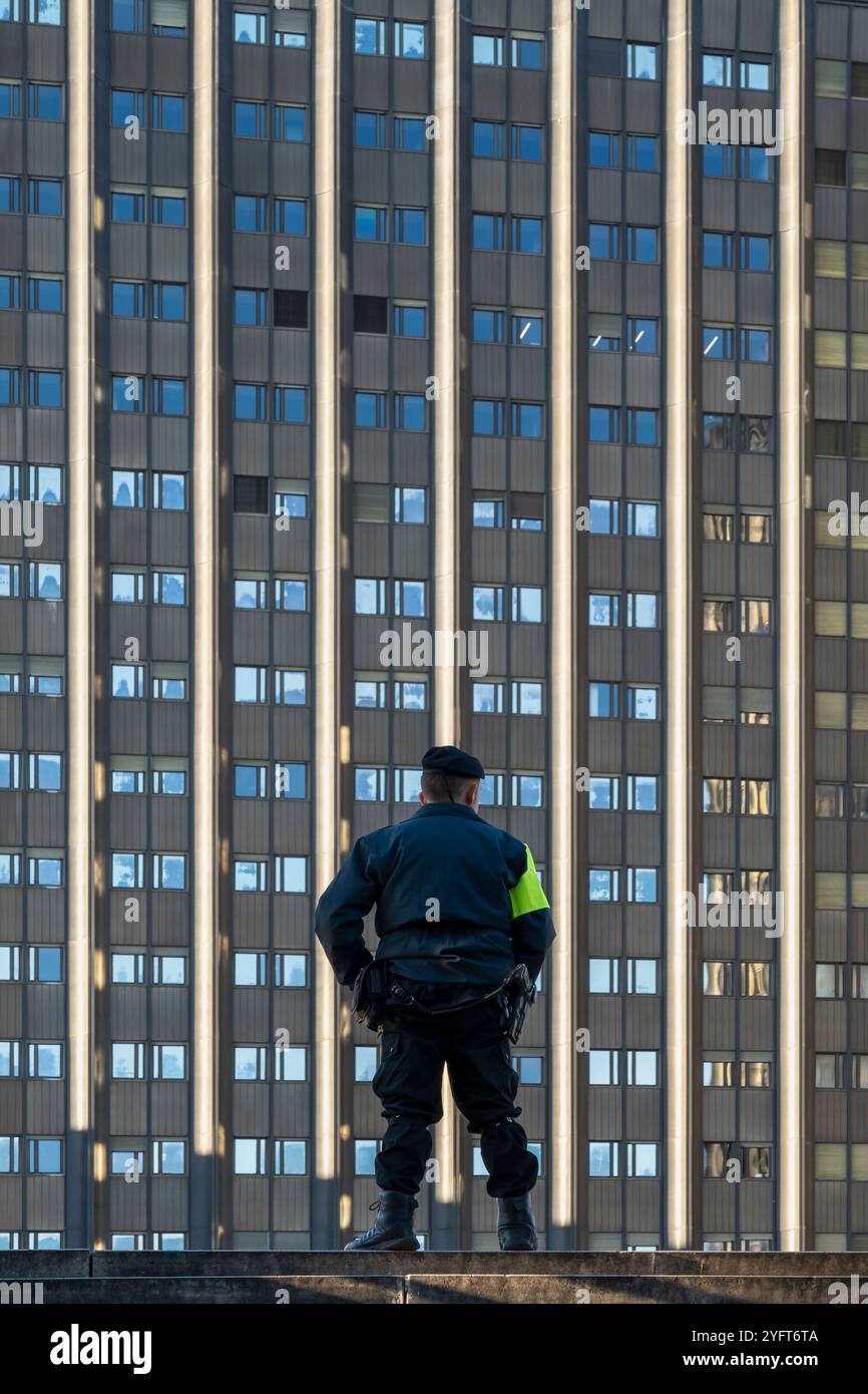 Un gardien de sécurité vêtu d'un uniforme professionnel, vu de derrière, se tient devant un immeuble de bureaux moderne. Sécurité, surveillance. Rome, Italie Banque D'Images
