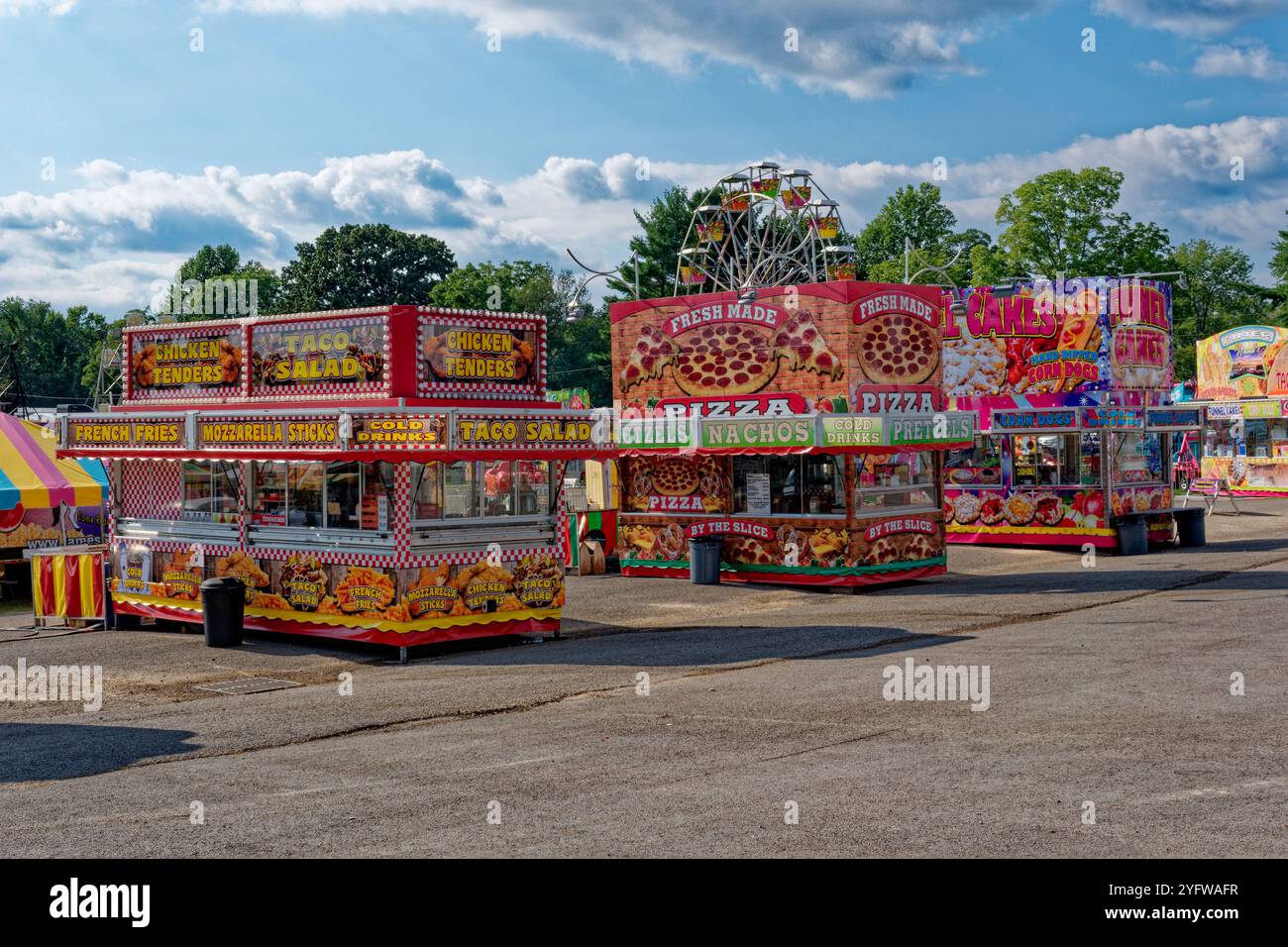 Remorques de concessions de nourriture et de boissons lumineuses et colorées à la foire annuelle du comté avec quelques manèges de carnaval en arrière-plan prêts à ouvrir sur un su Banque D'Images Remorques de concessions de nourriture et de boissons lumineuses et colorées à la foire annuelle du comté avec quelques manèges de carnaval en arrière-plan prêts à ouvrir sur un su Banque D'Images