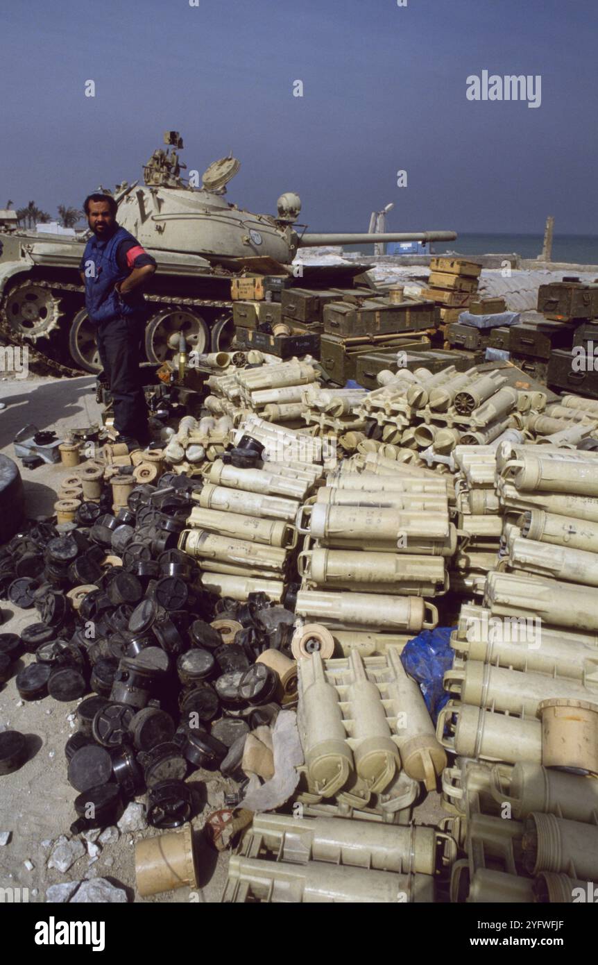 Première Guerre du Golfe : 10 mars 1991 Un soldat koweïtien veille sur un énorme stock de munitions irakiennes abandonnées, principalement des bombes de mortier et des mines terrestres, sur la plage d'Anjafa à Koweït City. En arrière-plan se trouve un char chinois de type 69 dans son revêtement. Banque D'Images
