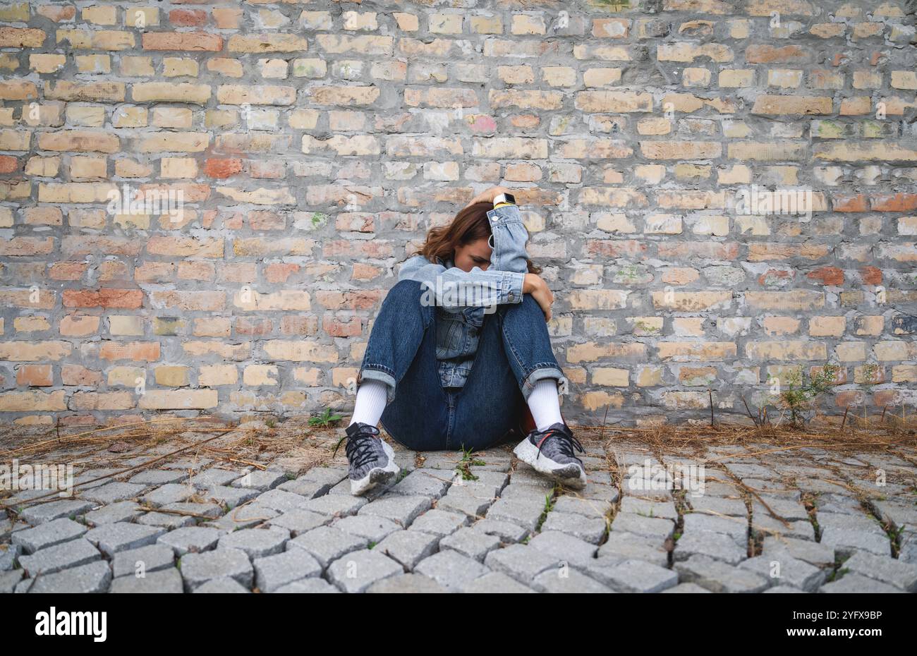 Femme déprimée se recourbant, assise sur le sol cachant son visage avec ses mains. Profonde détresse émotionnelle ou dépression. Toxicomanie. Banque D'Images