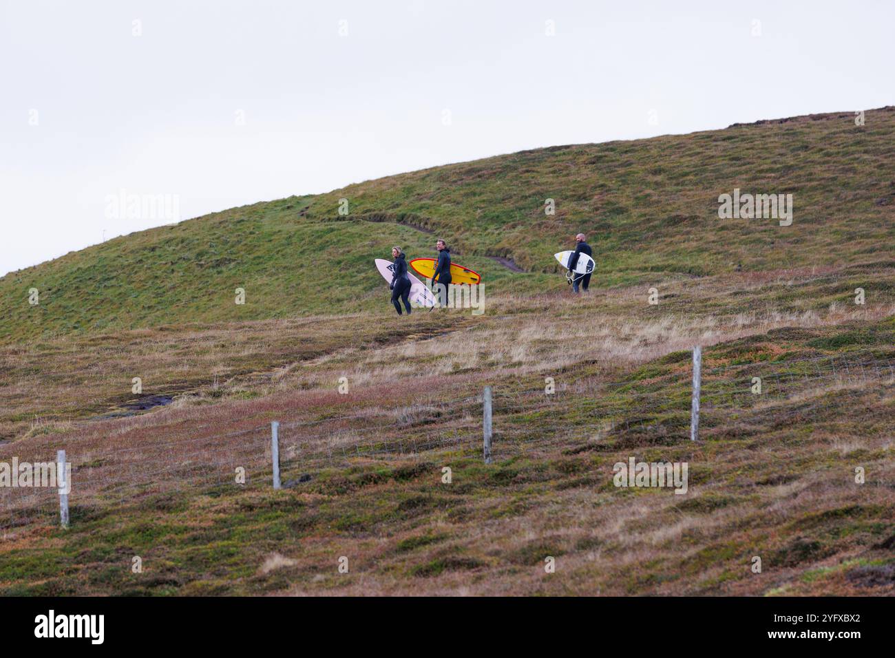 1er novembre 2024. Dunnet Head, Écosse. Deux surfeurs masculins et une surfeuse remontant un promontoire à Dunnet Head près de Thurso, en Écosse. Banque D'Images