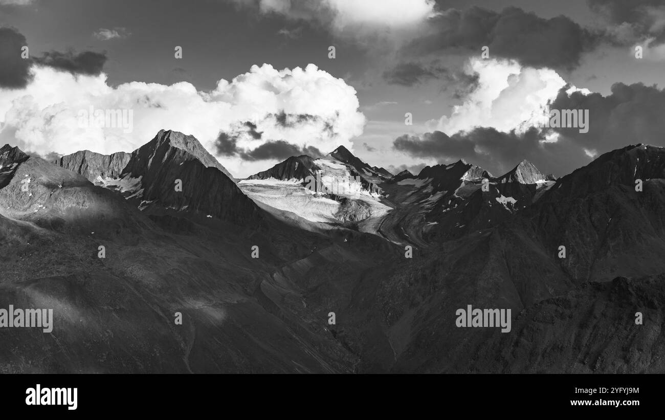 La lumière du soleil du soir projette des ombres sur les pics alpins accidentés, révélant leurs formes majestueuses sur fond de nuages tourbillonnants. Le paysage allie sérénité et grandeur, mettant en valeur la beauté intacte de la nature. Banque D'Images