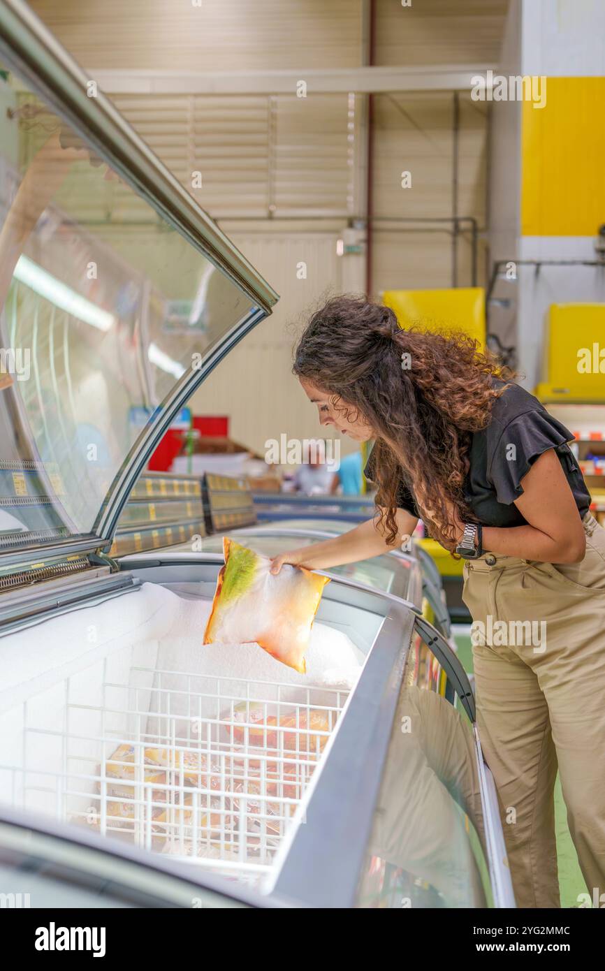 Femme d'âge moyen choisissant des aliments surgelés dans la section congélateur du supermarché Banque D'Images