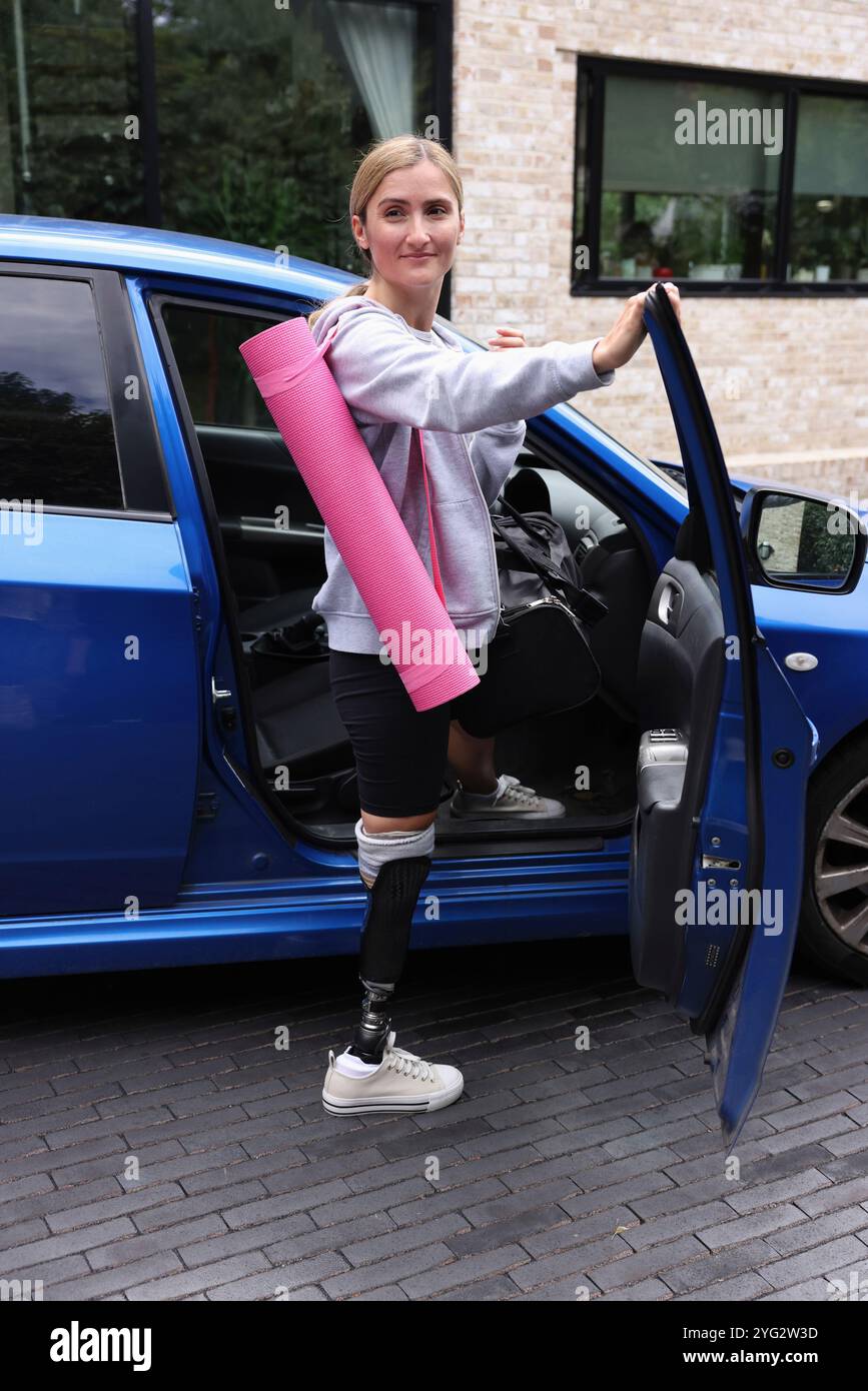 Femme blonde avec une jambe prothétique, tenant un tapis d'exercice et montant en voiture Banque D'Images