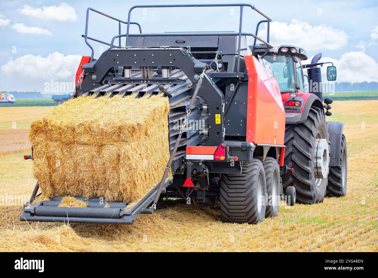 Pressage de foin avec un tracteur par un après-midi ensoleillé sur une vaste ferme au ciel bleu vif. Banque D'Images