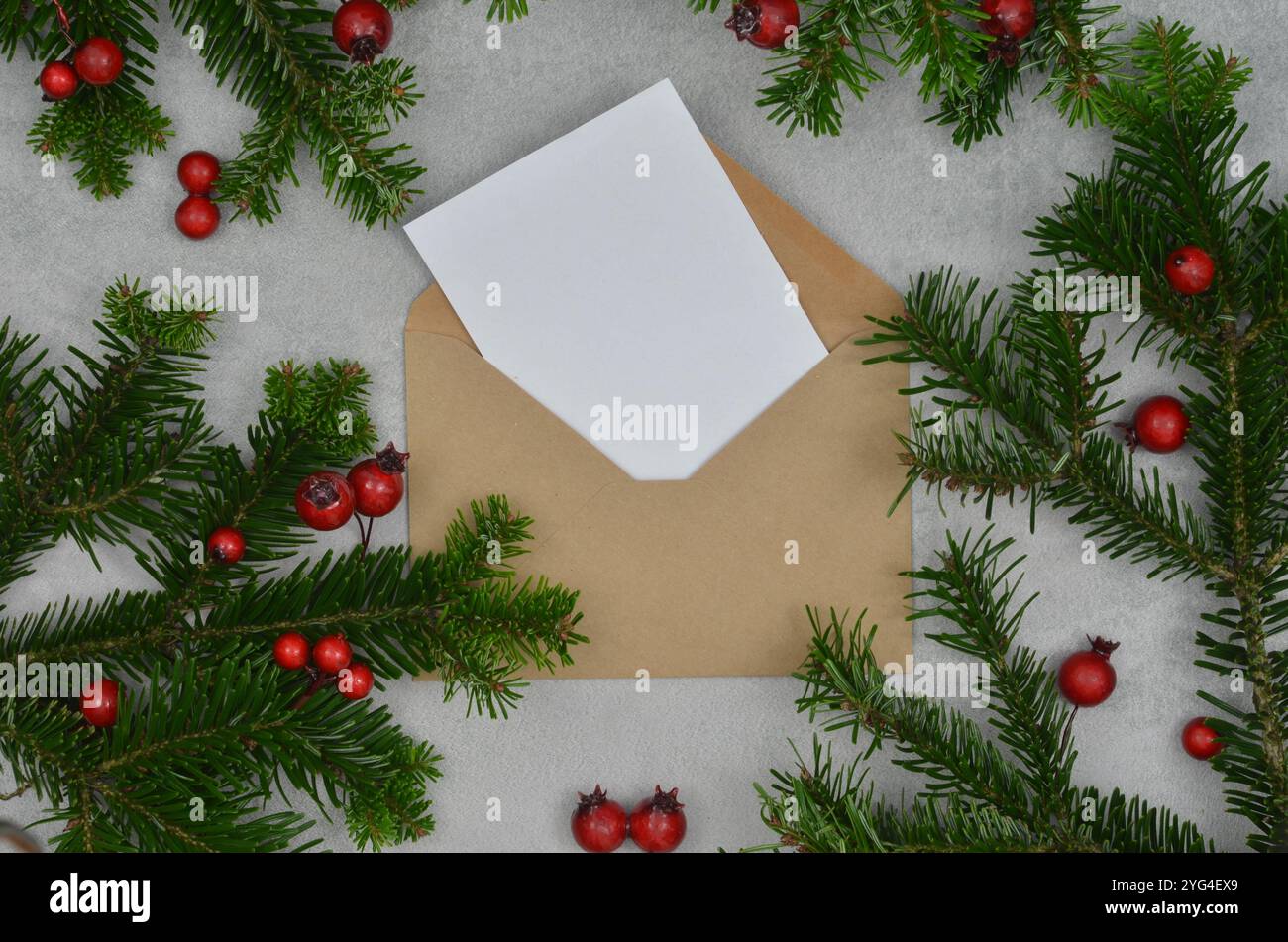 Carte vide et enveloppe entourée de décorations de Noël, branches d'arbre de Noël et fruits rouges, vue de dessus. Banque D'Images
