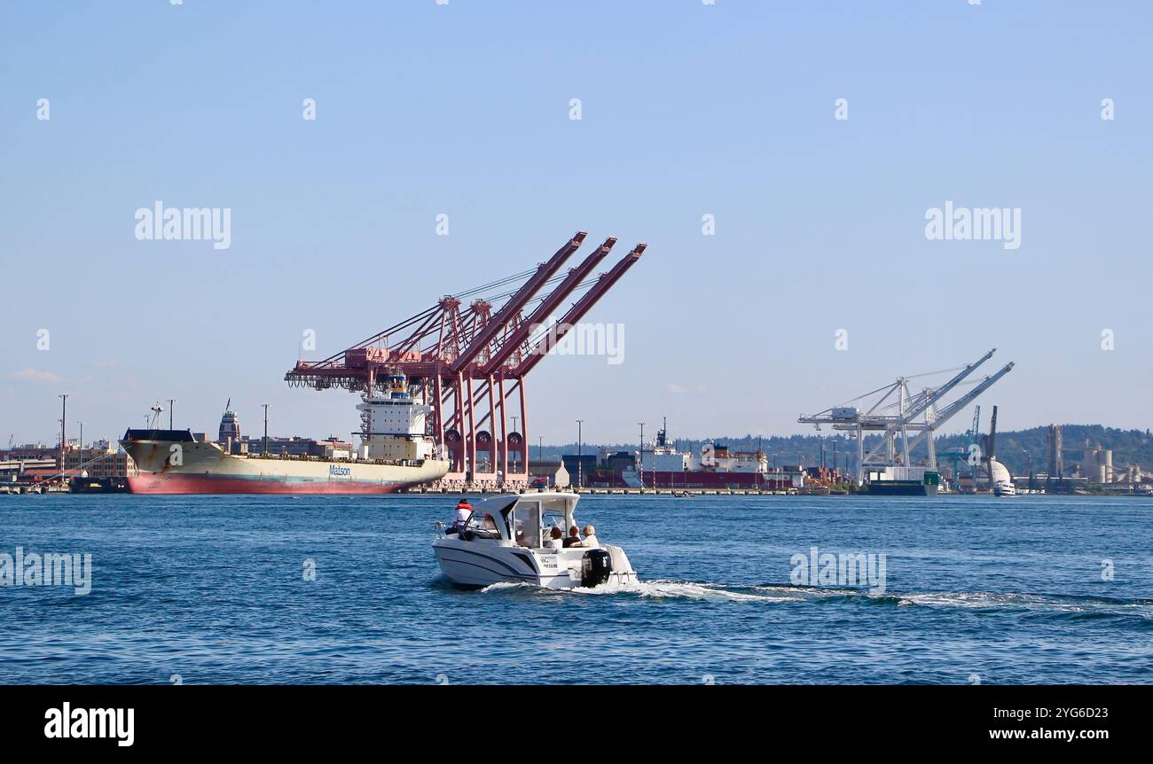 Container Ship Maunalei amarré au quai éclipsé par d'énormes grues avec un bateau à moteur de passage au premier plan Seattle Washington State USA Banque D'Images