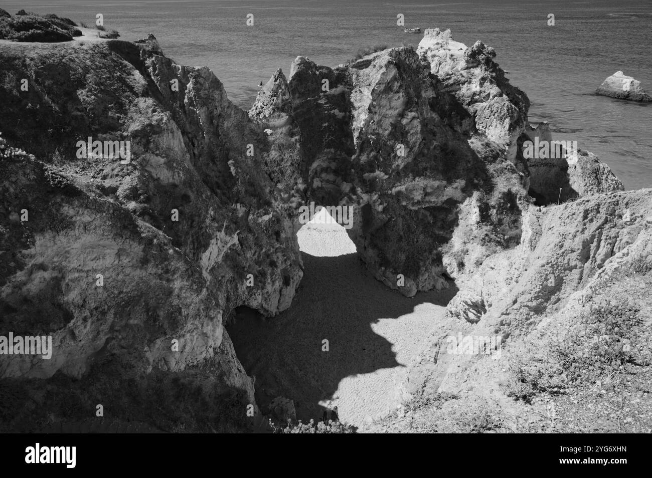 Vue en noir et blanc de la voûte rocheuse naturelle à praia da rocha, encadrant une plage isolée et l'océan dans un contraste frappant Banque D'Images