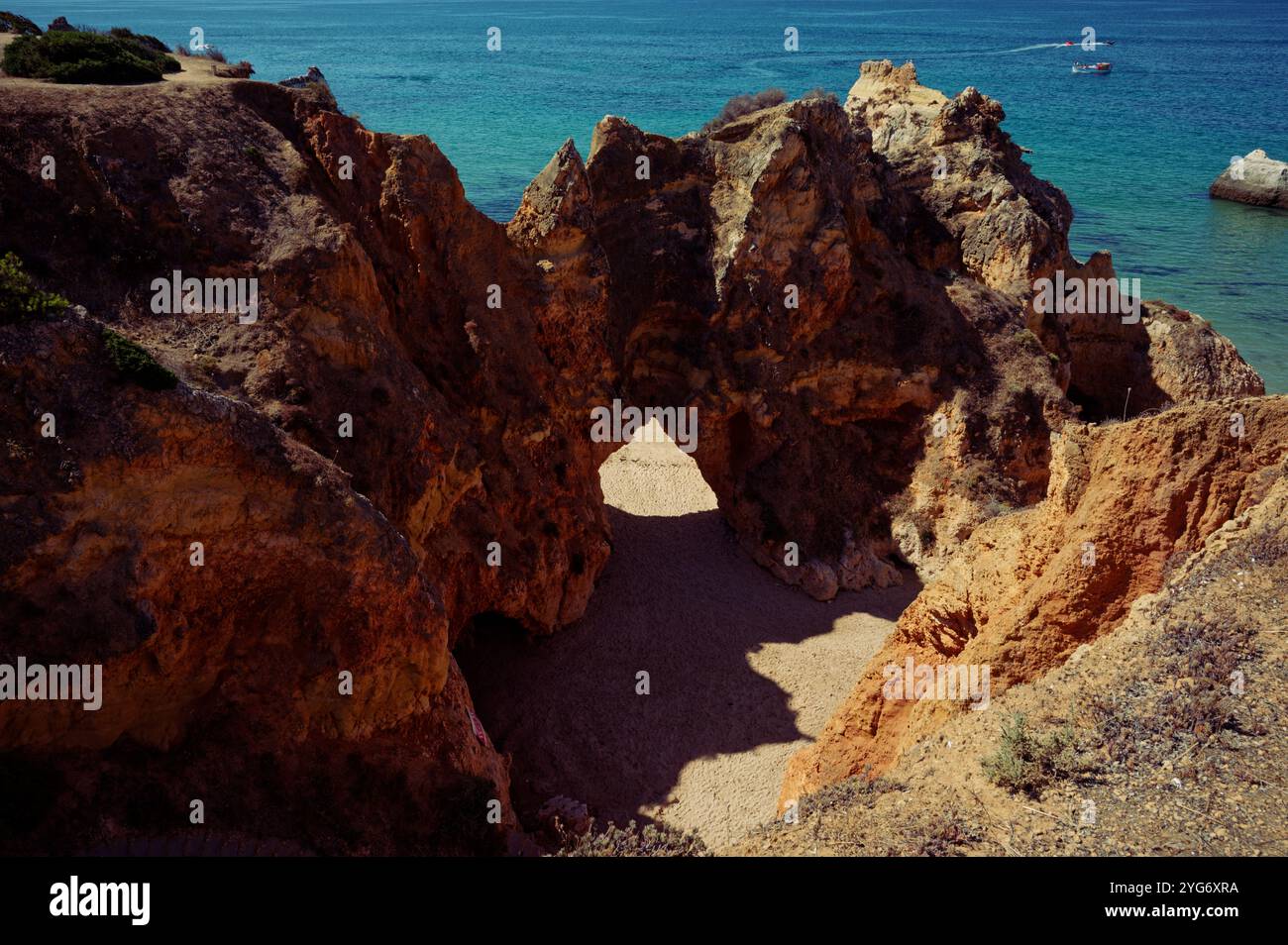 Arche rocheuse menant à une plage, baignée de soleil et entourée de blues océaniques vibrants Banque D'Images