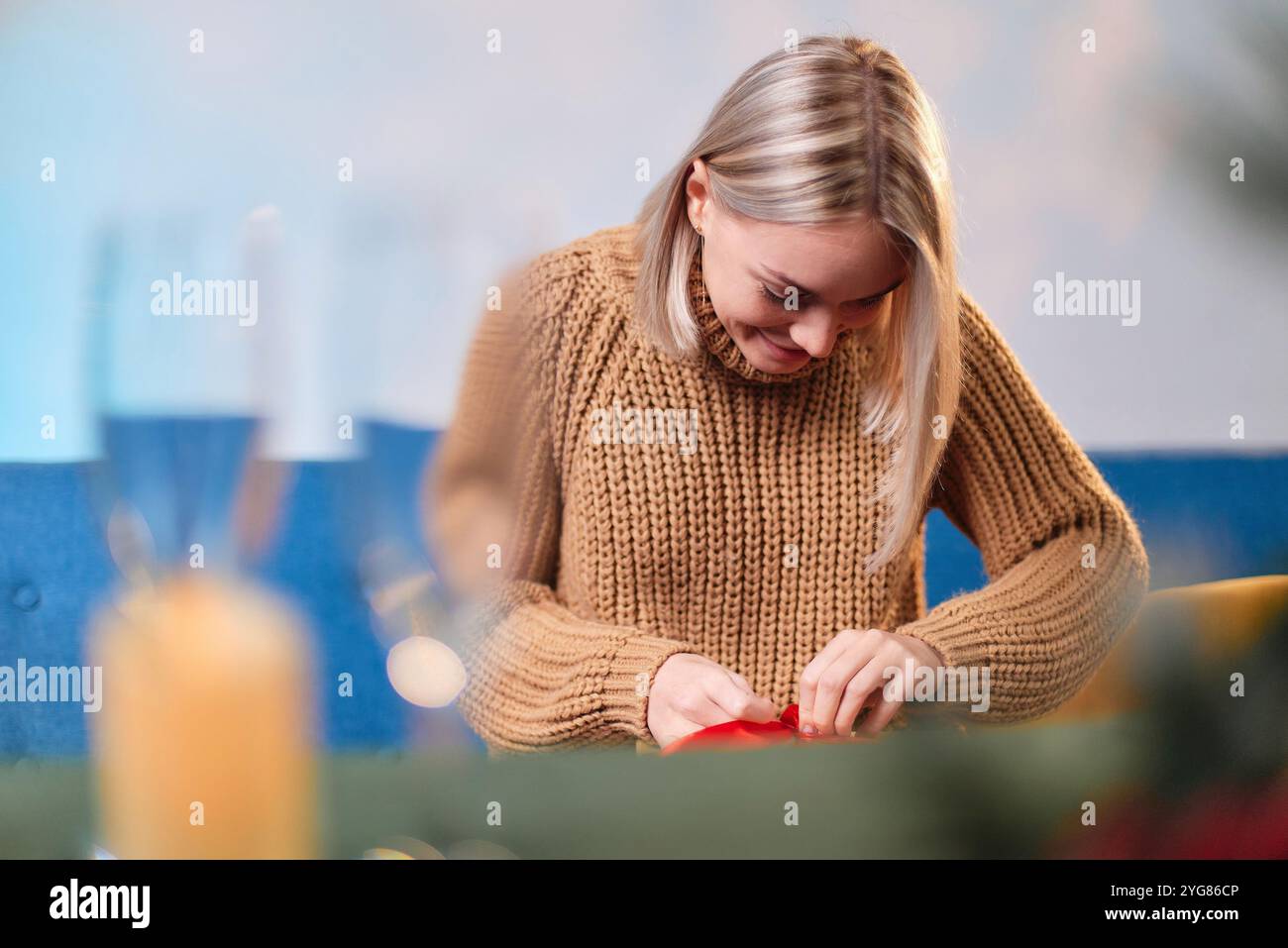 Jeune femme enveloppant un cadeau de Noël à la maison, souriant et attachant un ruban rouge sur un cadeau Banque D'Images